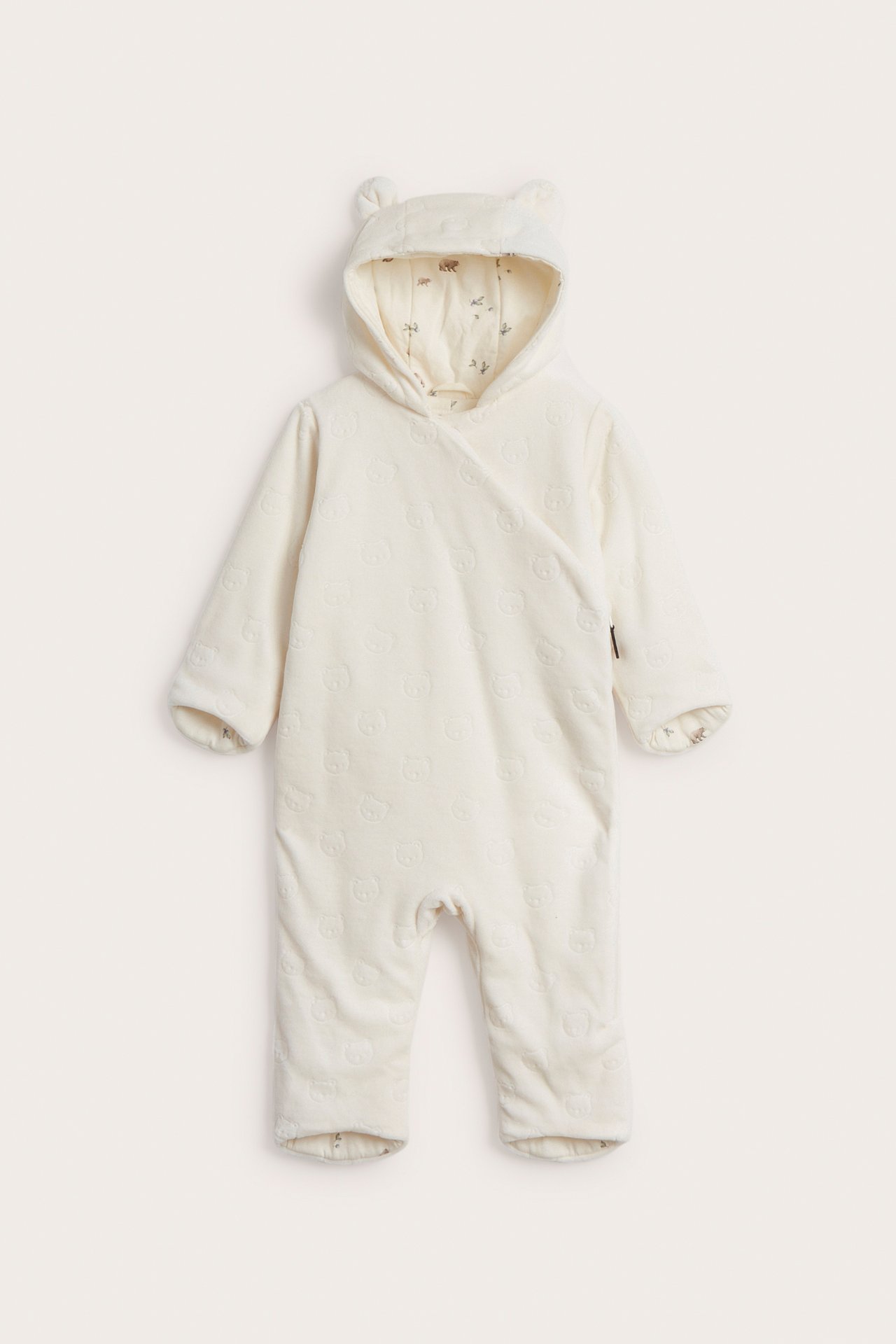 Front view of an offwhite velour baby coverall with embossed pattern, hood with ears, and printed lining.