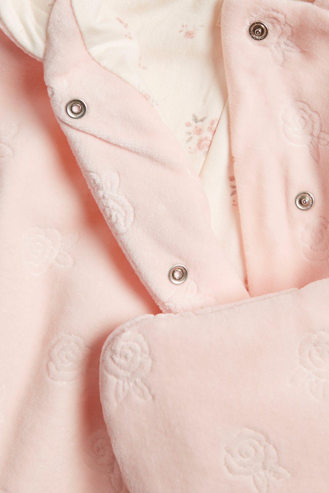 Nahaufnahme eines rosa Velours-Babyoveralls mit geprägten Rosen, Druckknöpfen und Blumenfutter.