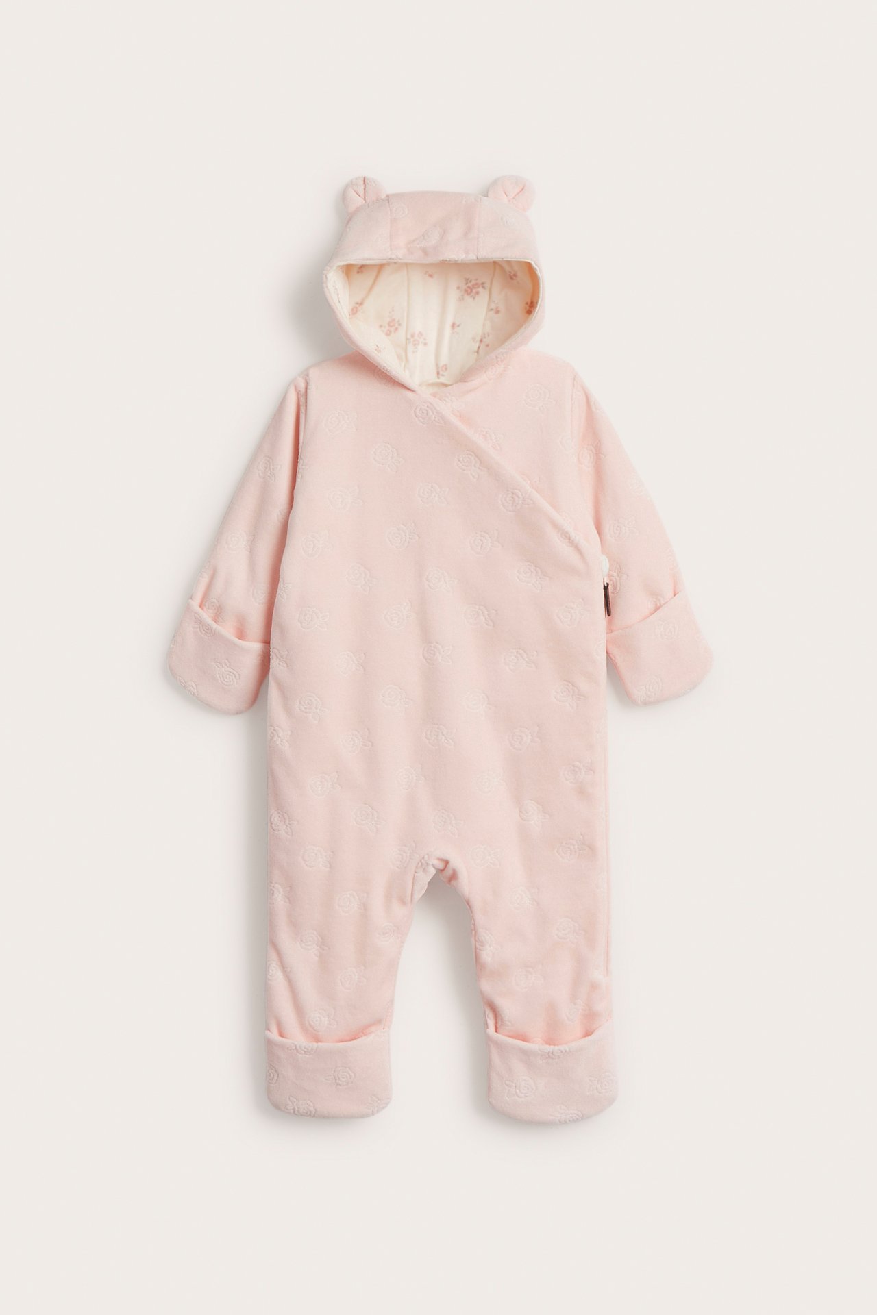 Vorderansicht: Rosa Velour-Babyoverall mit Prägemuster, Kapuze mit Ohren und umklappbaren Bündchen.