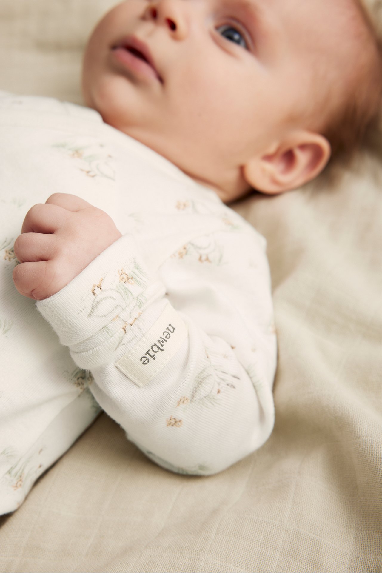 Nahaufnahme eines Babys in einem cremefarbenen gerippten Wickelbody aus Bio-Baumwolle mit Muster.