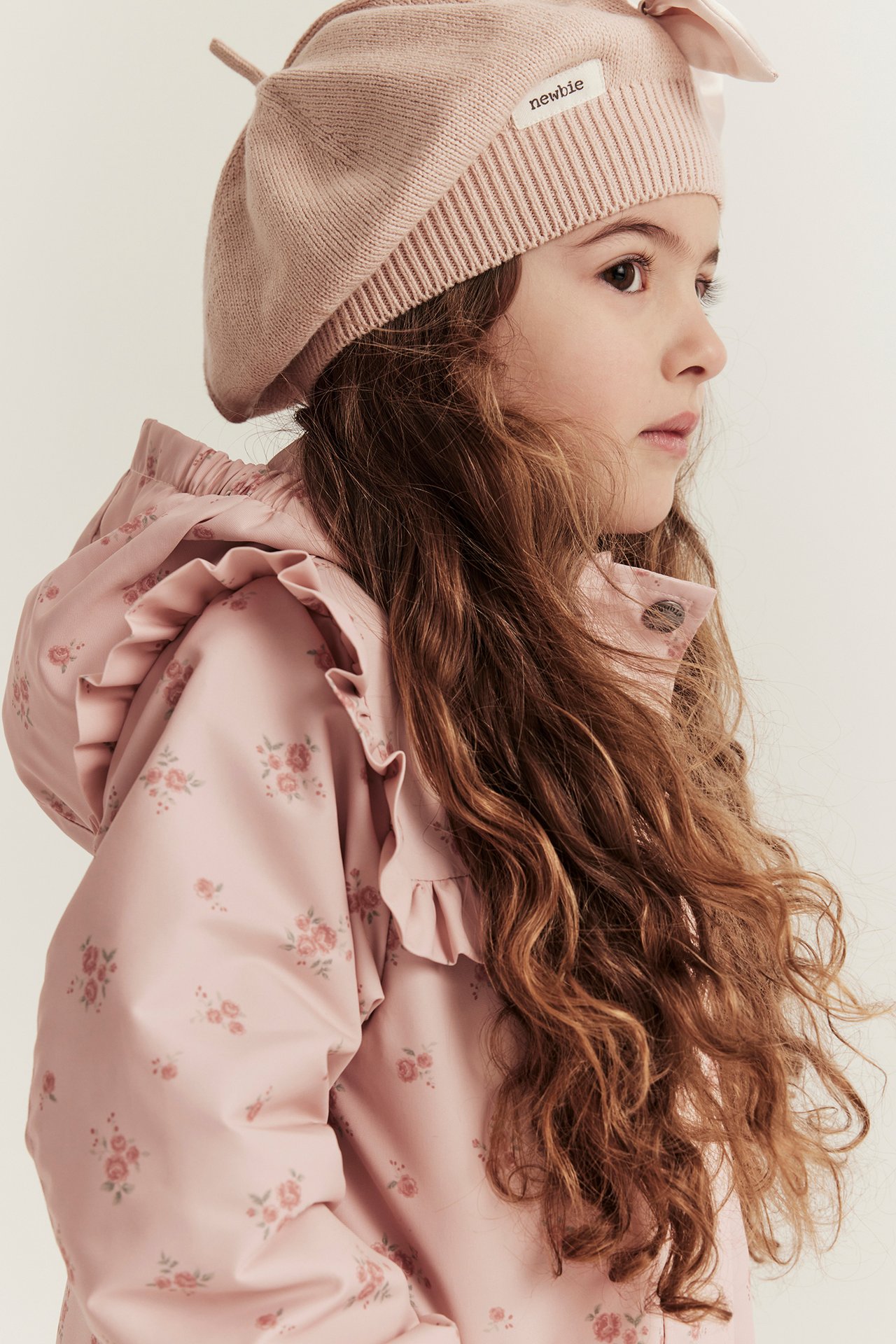Nahaufnahme Seitenansicht eines Kindes in einer hellrosa geblümten Rüschenjacke und einer rosa Strickmütze.