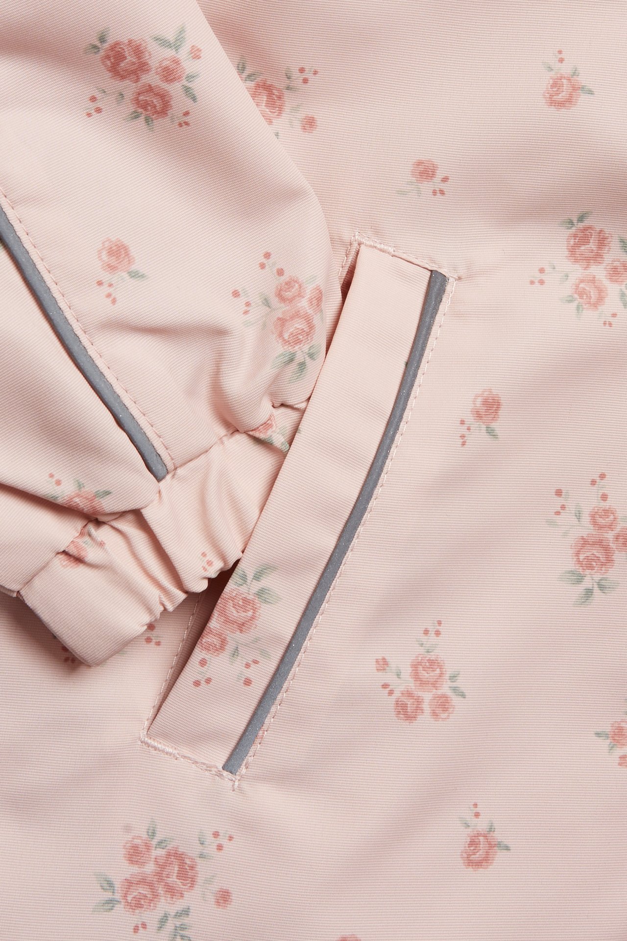 Nahaufnahme einer hellrosa Blumen-Kinderjacke mit reflektierendem Detail an der Tasche und elastischem Bündchen.