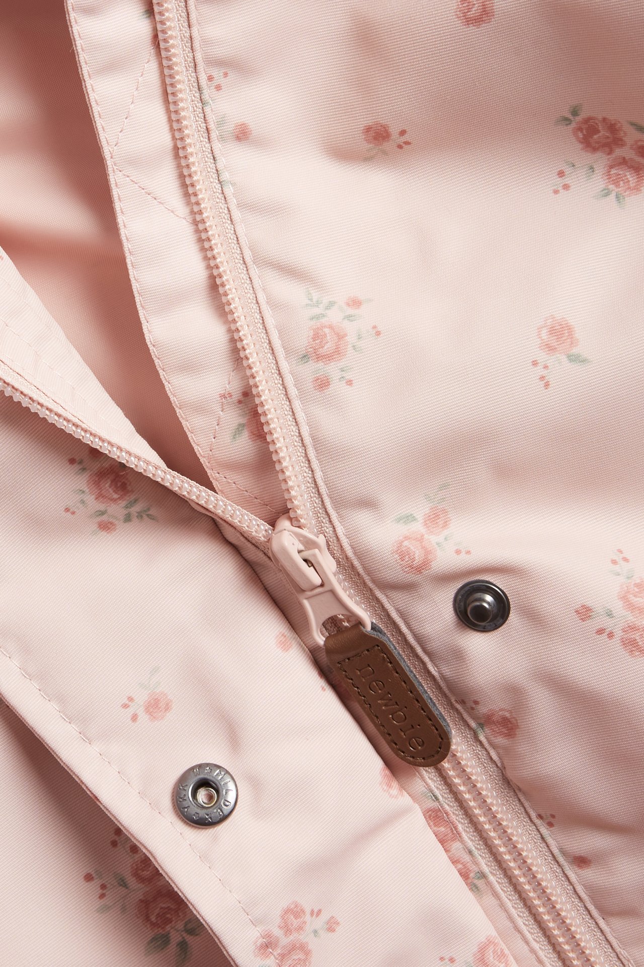 Nahaufnahme einer hellrosa Blumenjacke mit Reißverschluss und Druckknöpfen vorne.