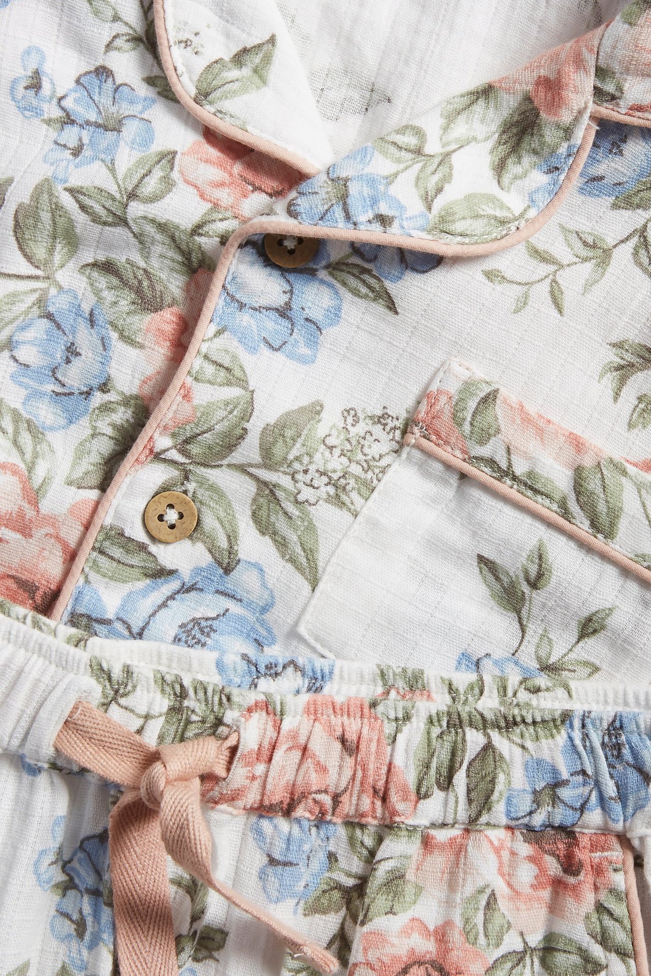 Close-up: off-white cotton floral pajama set with blue and pink flowers, button-front top, drawstring pants.