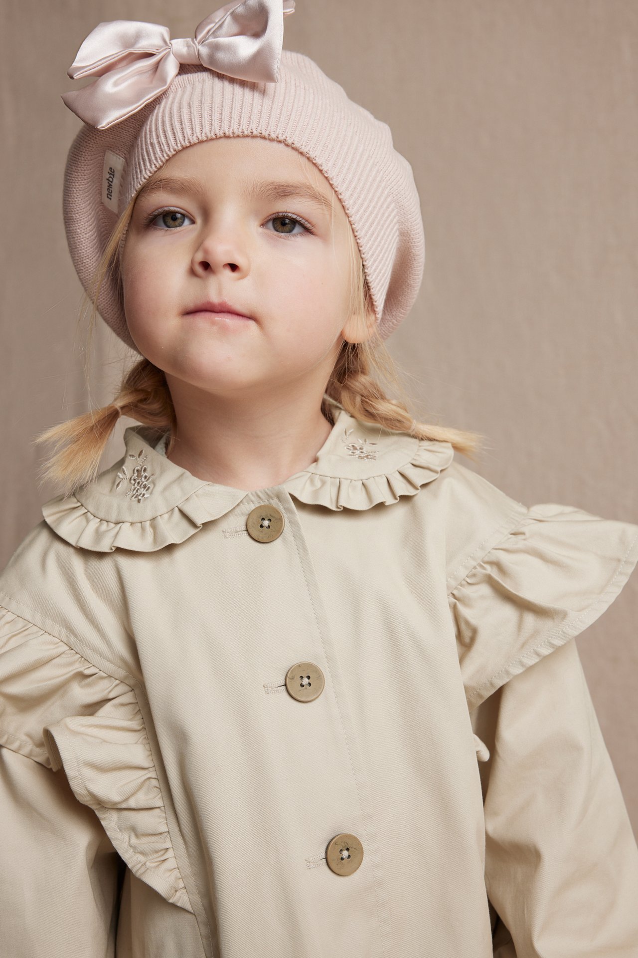 Beige cotton ruffled jacket and a pink knitted beret with a bow on a kid.