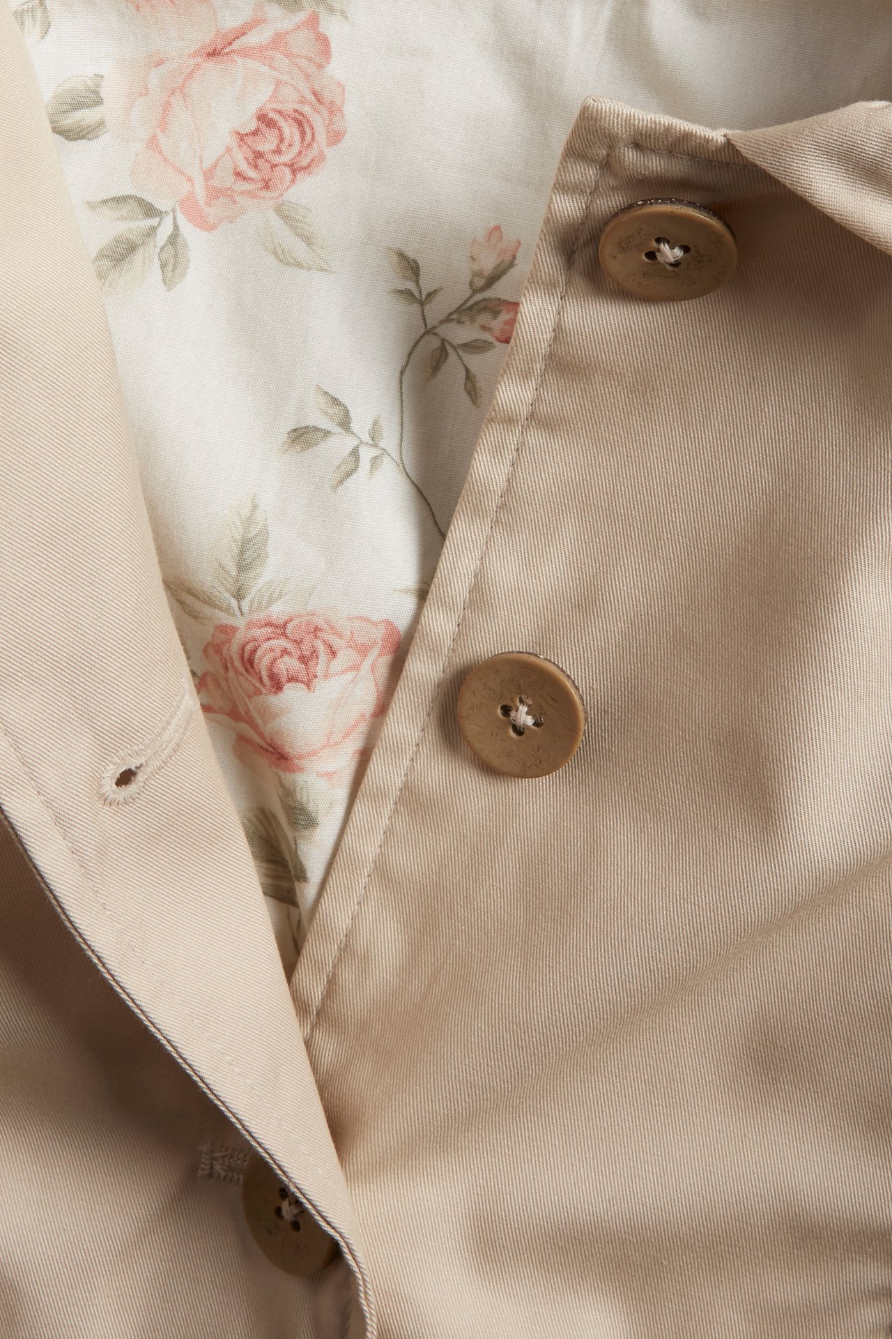Close-up of a beige cotton jacket with brown buttons and a pink floral lining visible at the opening.