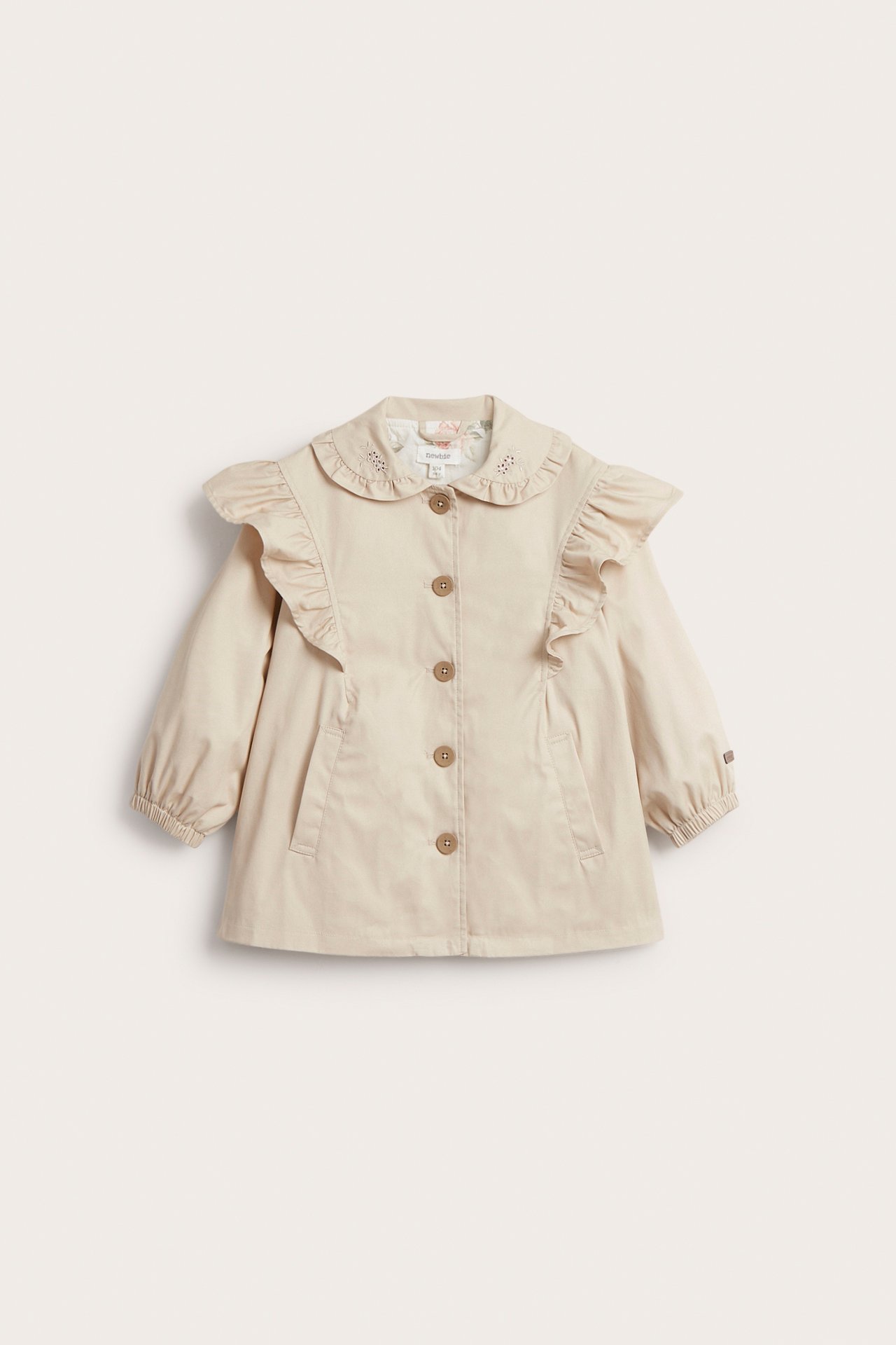 Front view: Kid's beige cotton jacket with embroidered ruffled collar, button front, and ruffled shoulders.