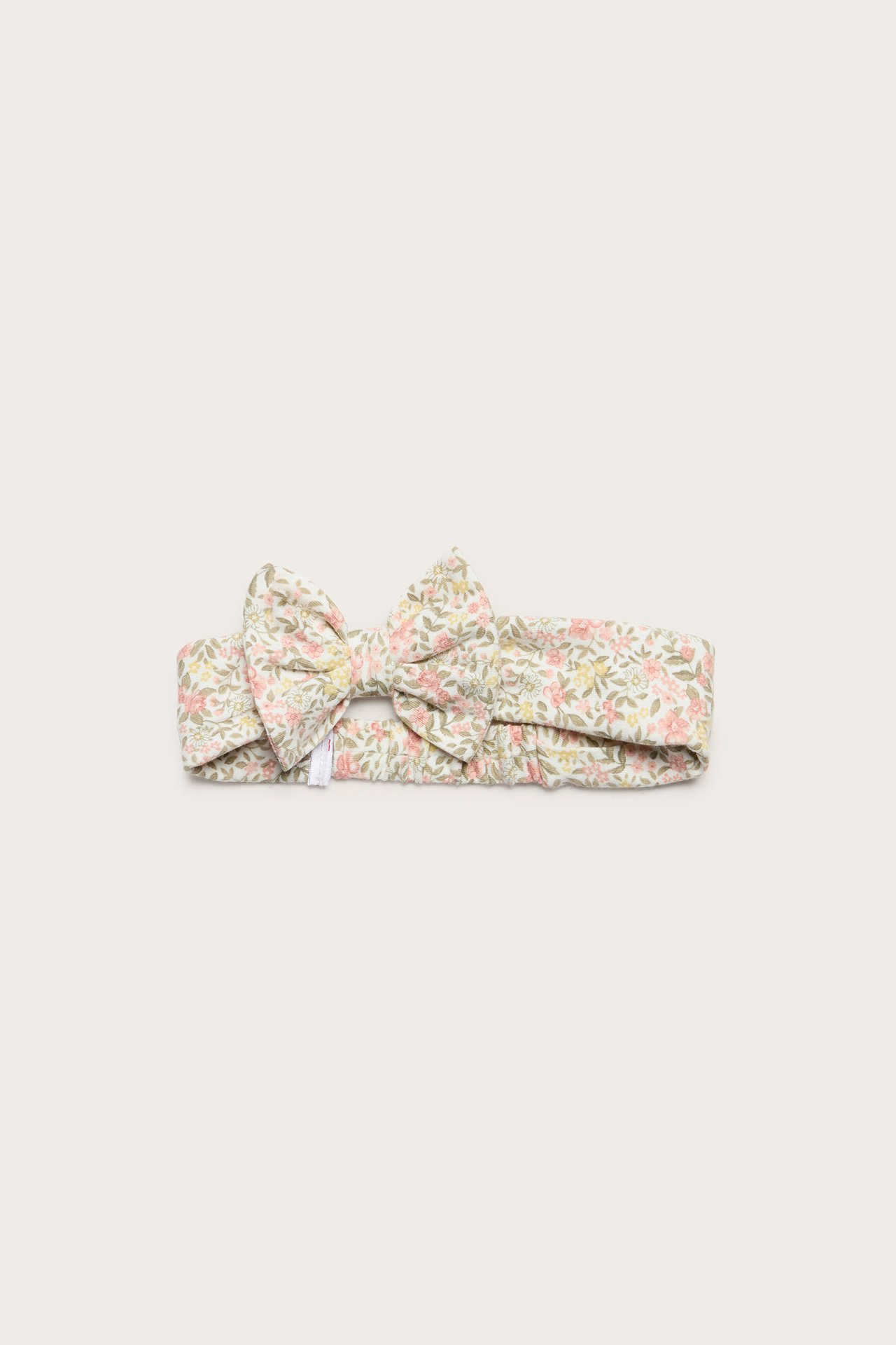 Front view: Off-white cotton jersey headband with a pink and green floral pattern and a bow.