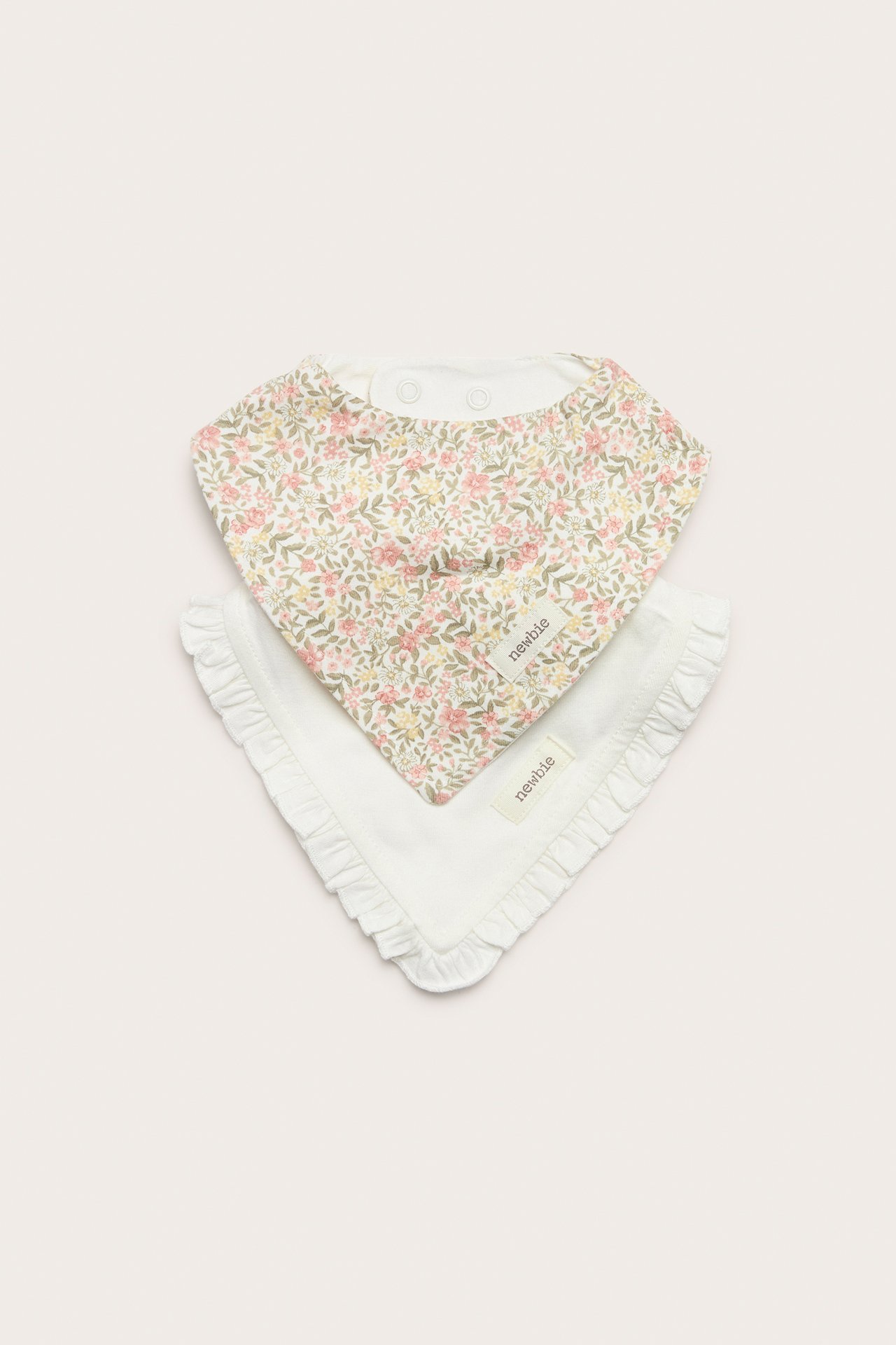 Front view of two cotton baby bibs: one floral, one off-white with ruffle edge, both with snaps.