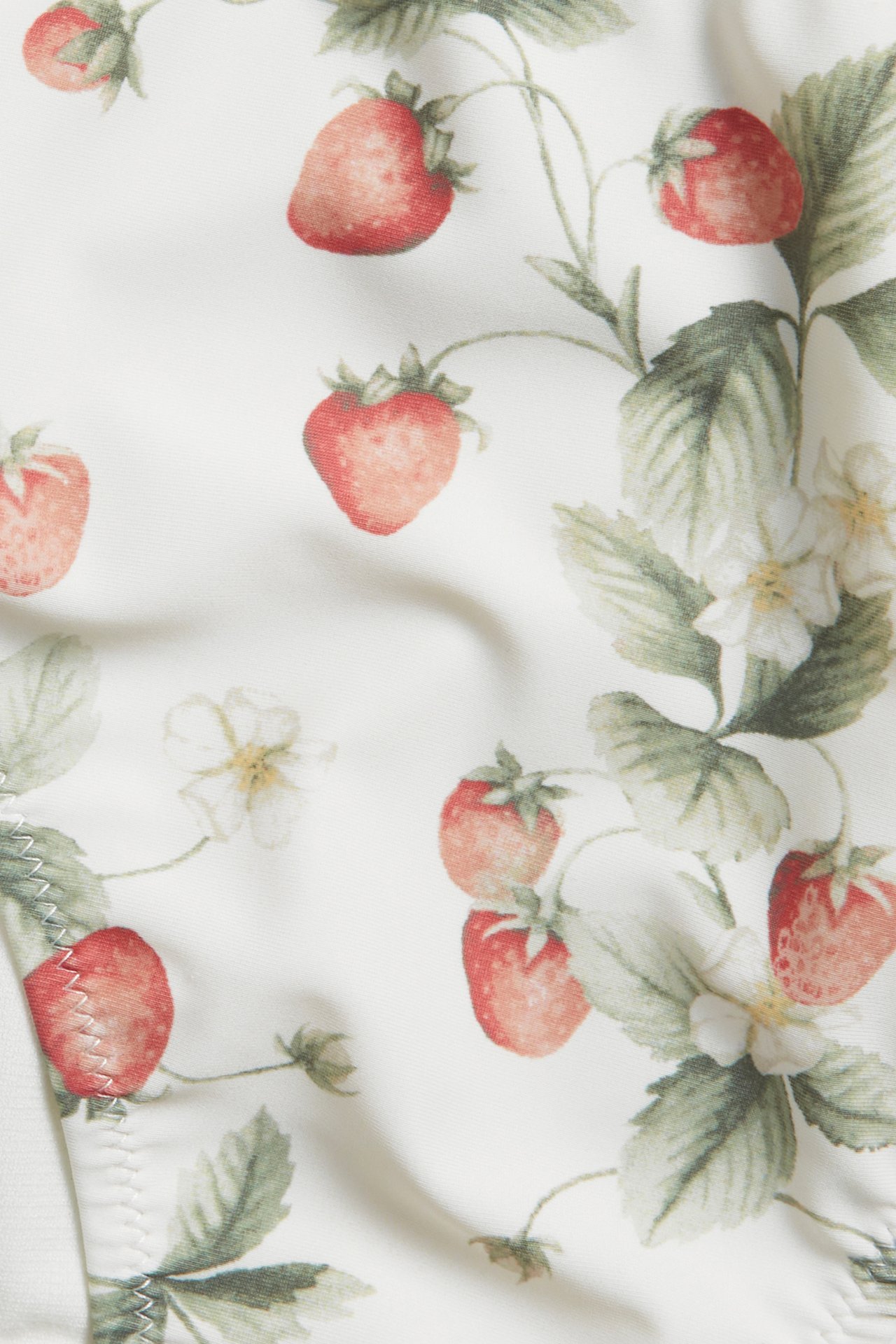Close-up of an offwhite bikini bottom with a red strawberry and floral pattern.