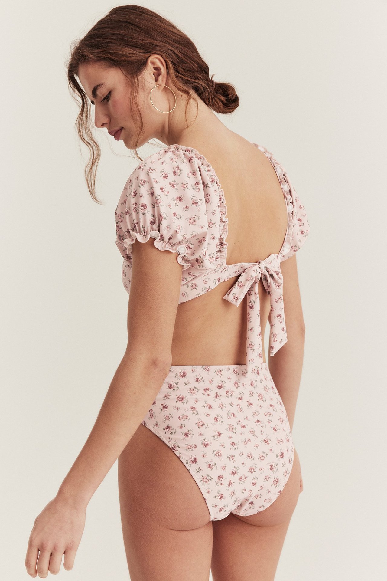 Schräge Rückenansicht einer Frau in rosa geblümter High-Waist-Bikinihose und passendem Puffärmel-Oberteil.