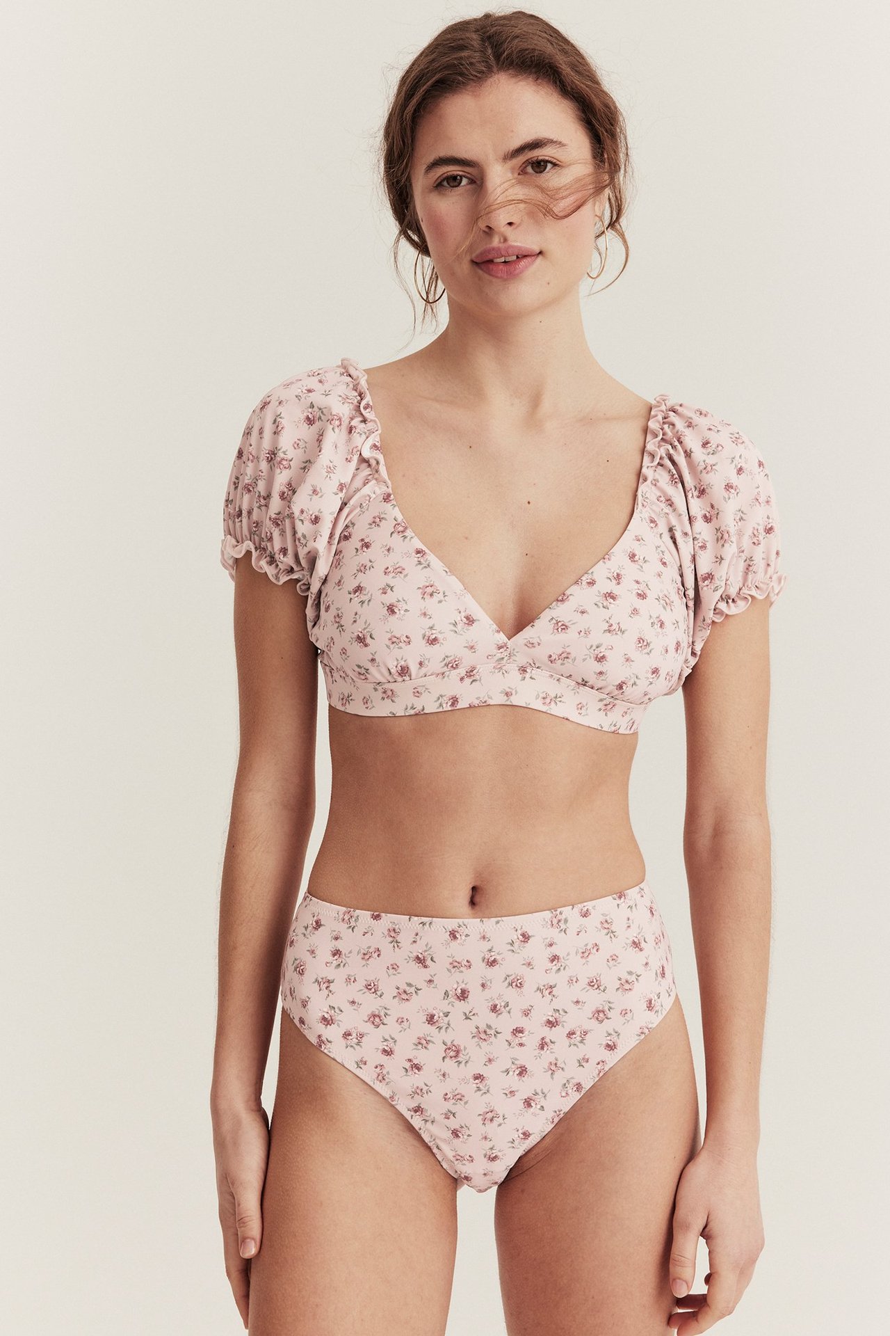 Vorderansicht einer Frau in rosa geblümter High-Waist-Bikinihose und passendem Bikinioberteil mit Rüschenärmeln.