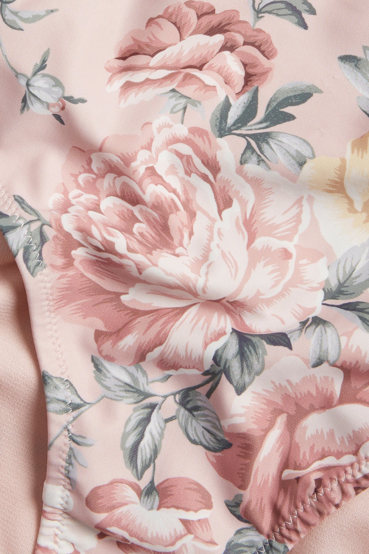 Close-up of a pink floral bikini bottom fabric, featuring large light pink and yellow flowers with green leaves.