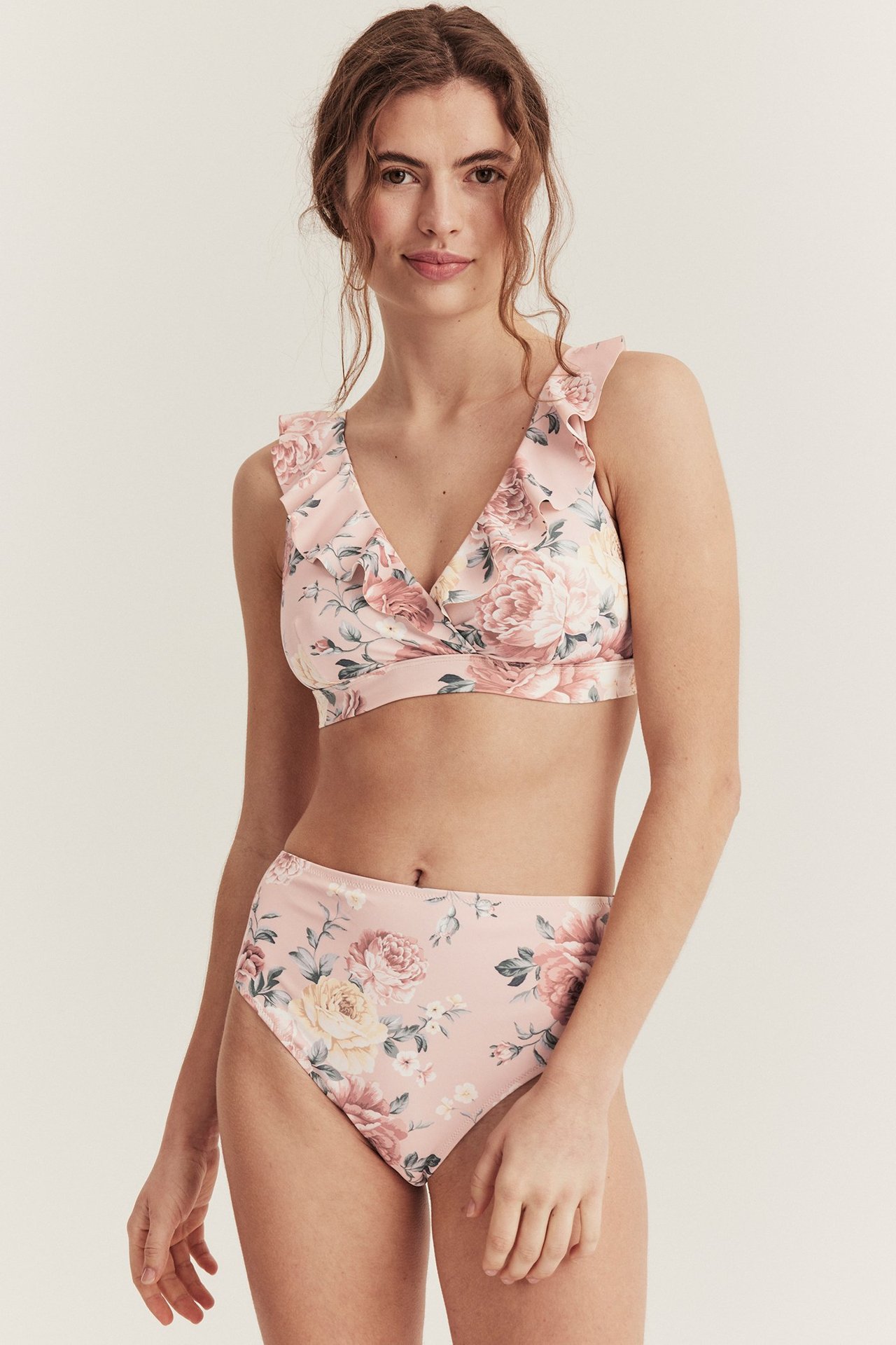 Vorderansicht einer Frau in rosa geblümtem Bikinislip mit hoher Taille und passendem Rüschen-Bikinioberteil.