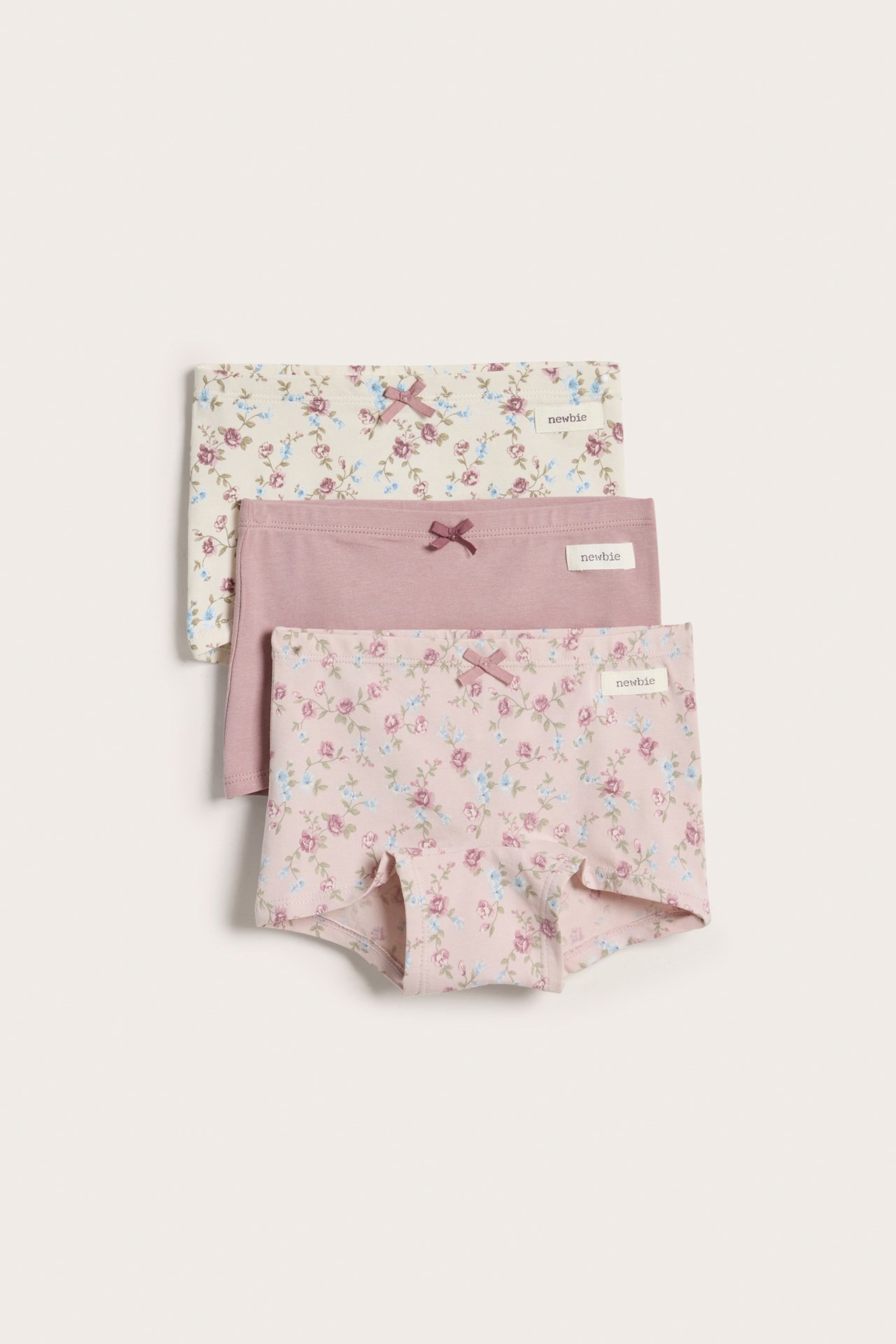 Front view of three stacked kid's jersey hipster briefs: two floral patterned, one solid pink, all with bows.