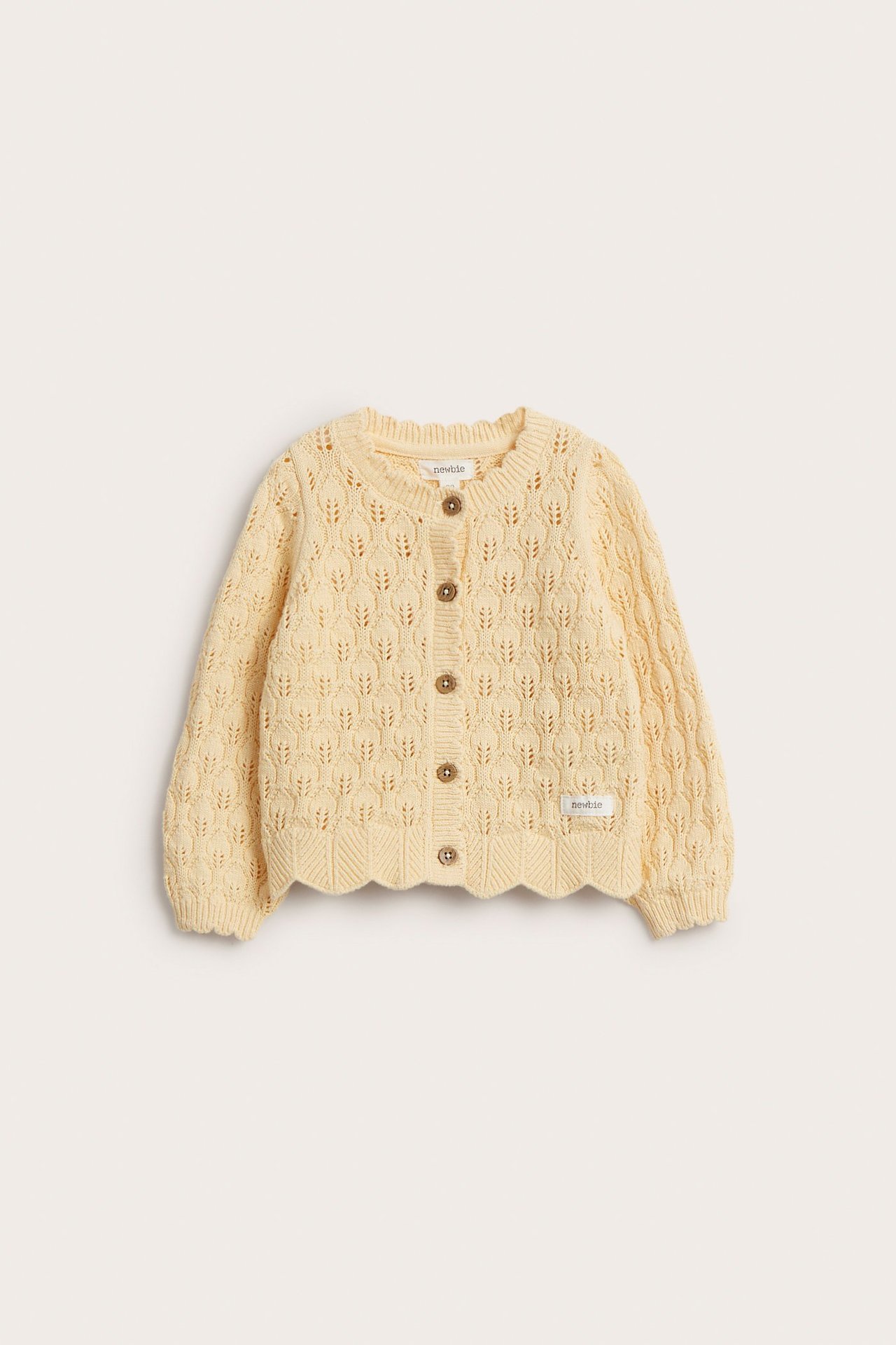 Front view of a baby's light yellow pattern-knitted cotton cardigan with brown buttons and scalloped edges.