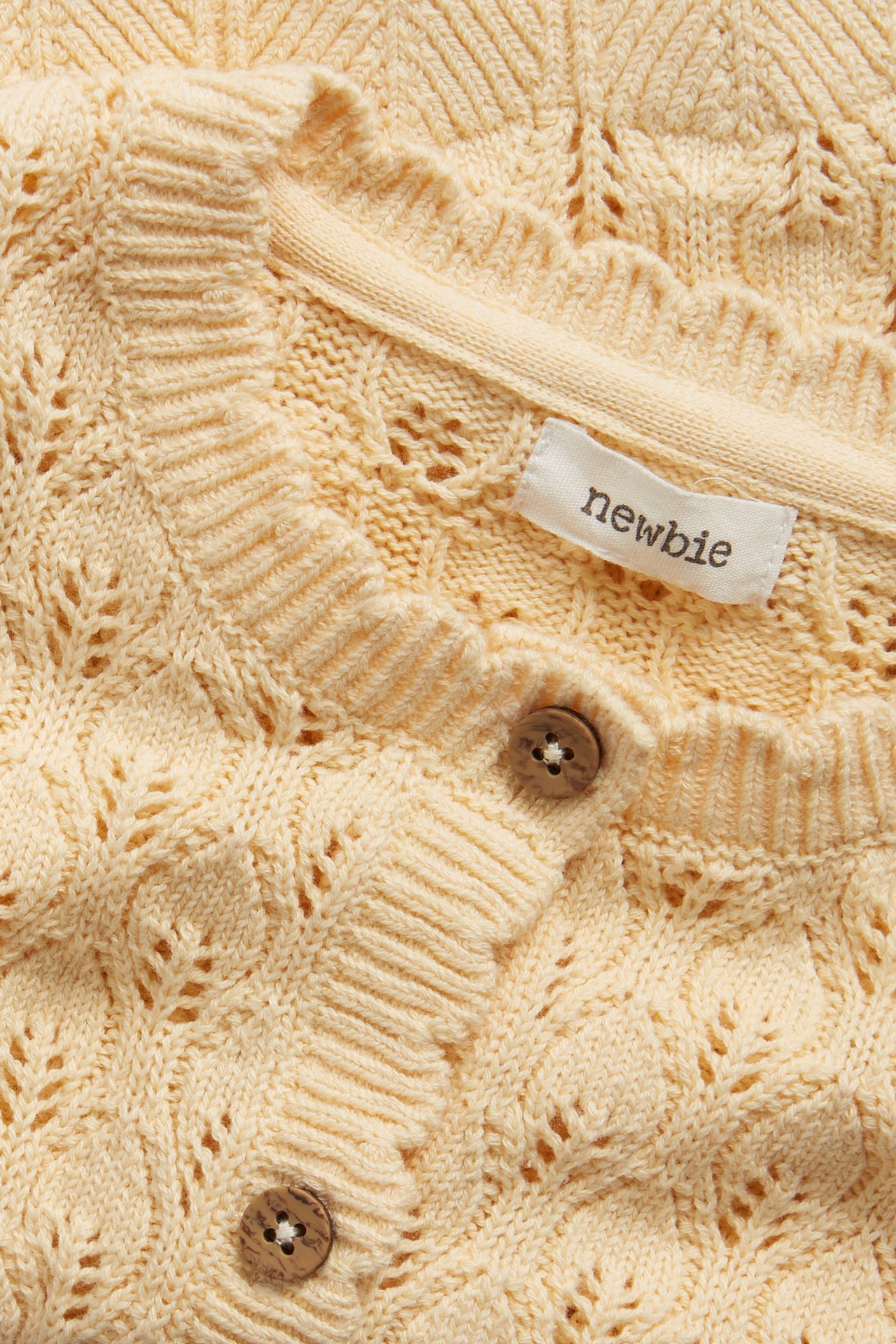 Close-up of a light yellow pattern-knitted baby cardigan made of cotton with brown wooden buttons.