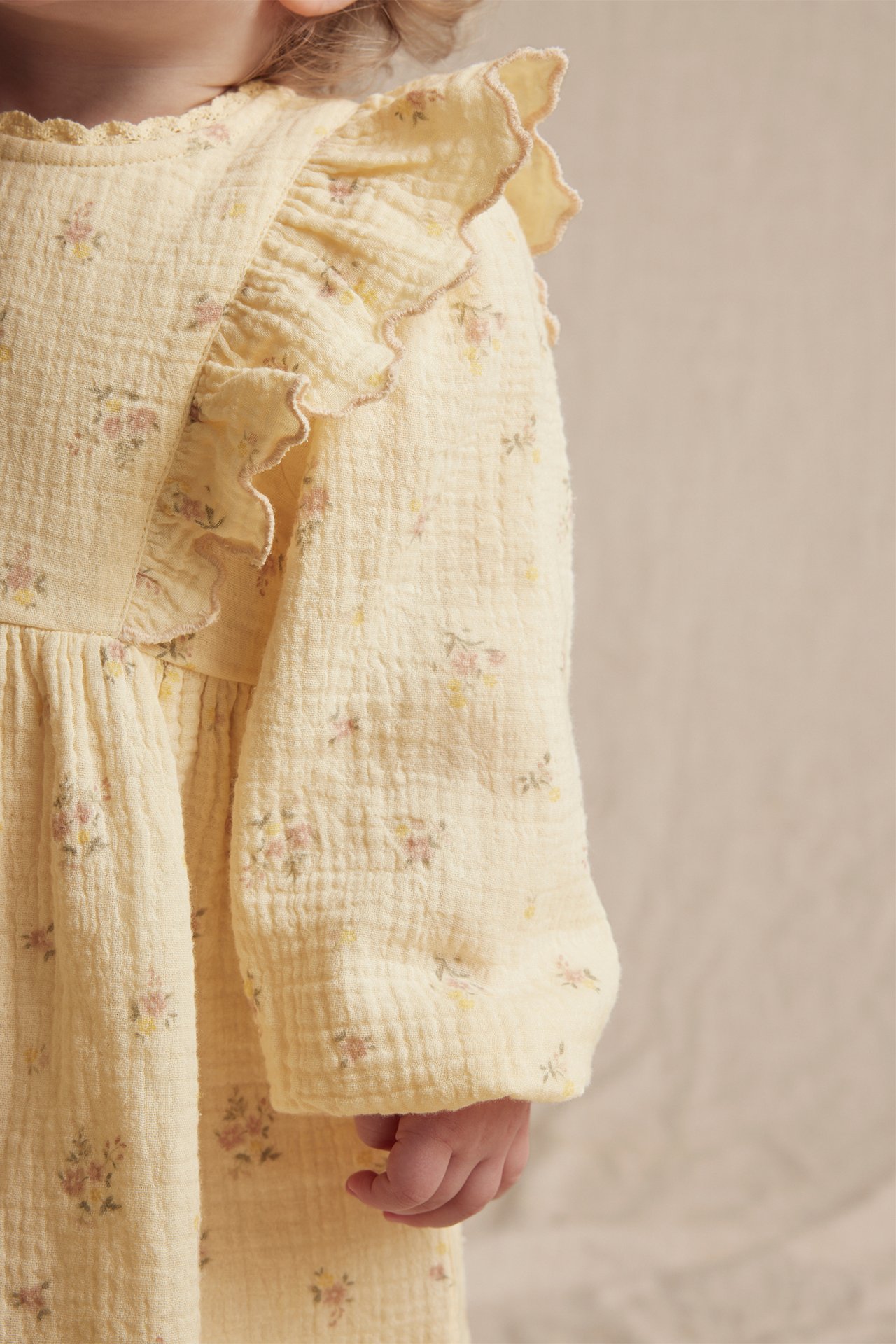 Close-up of a baby wearing a yellow floral crumpled cotton dress with ruffled puff sleeves.