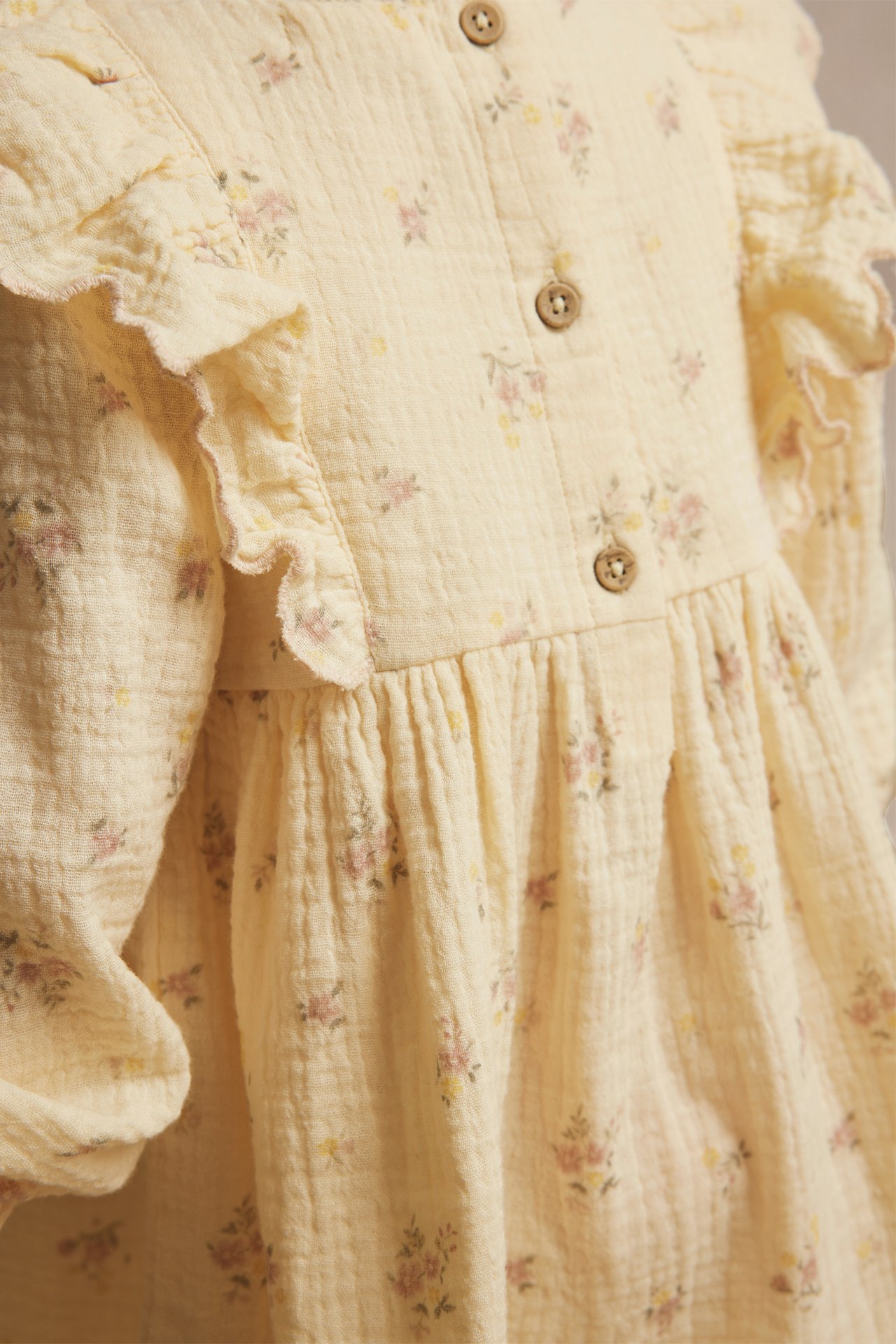 Close-up of a yellow crumpled cotton dress with a floral pattern, ruffles, puff sleeves, and buttons.