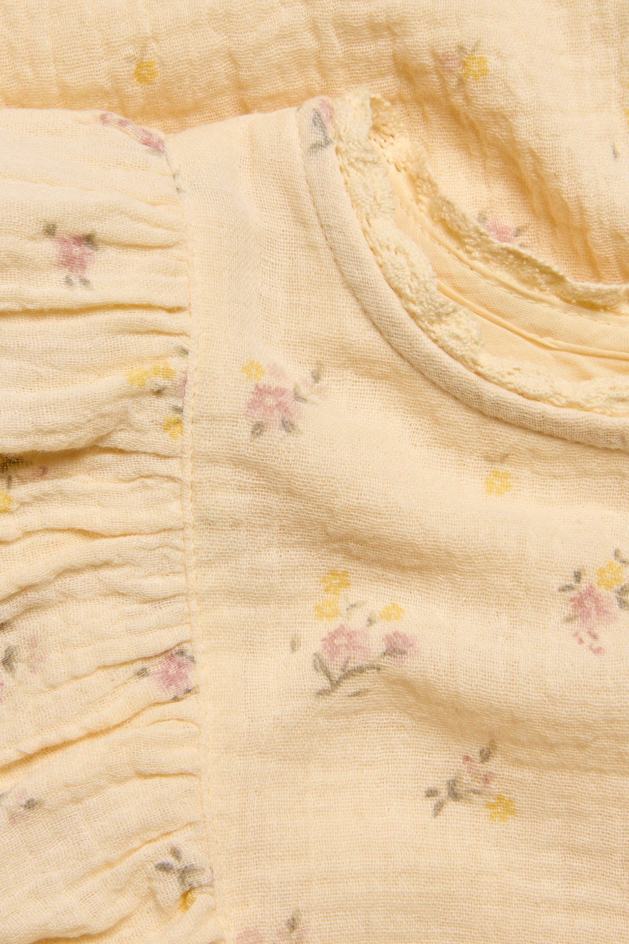 Close-up: yellow organic cotton crumpled dress with pink/yellow floral print, ruffled sleeve, lace neckline.