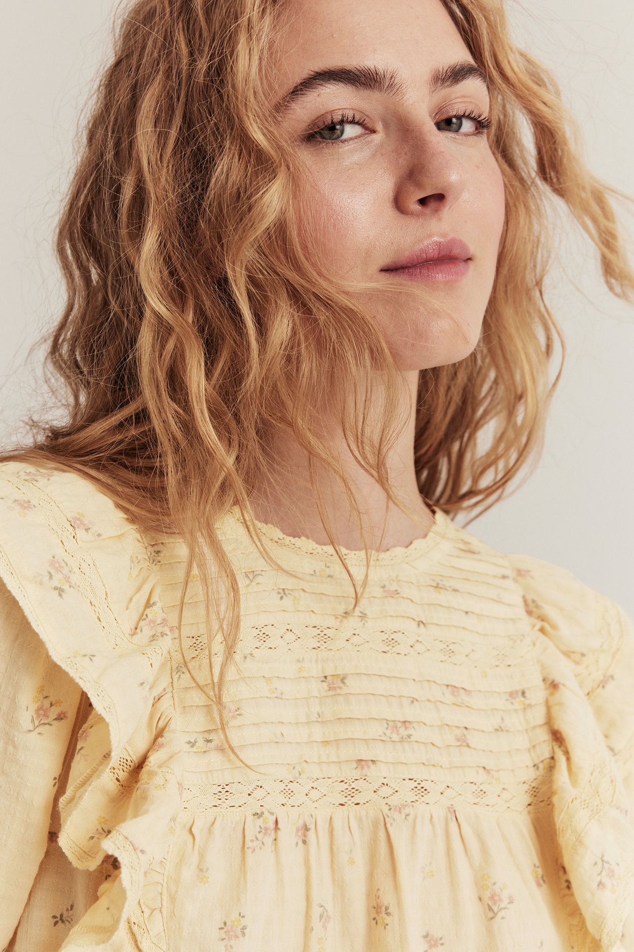 Close-up of a woman in a yellow floral blouse with lace-decorated ruffles and pintucks on the front.