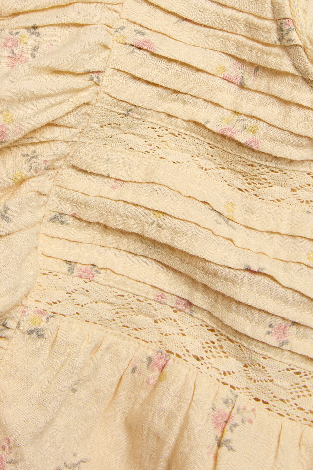 Close-up of a light yellow cotton blouse with a small floral pattern, pintucks, and lace inserts.