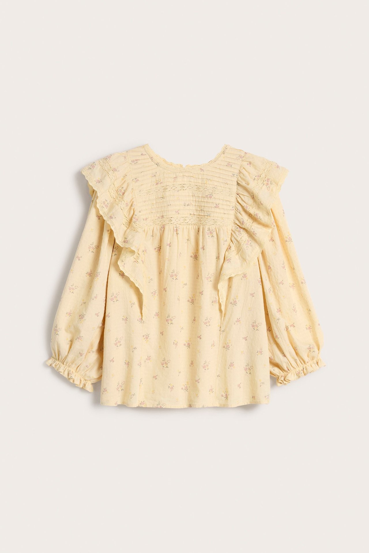 Front view of a woman's yellow floral cotton blouse with lace-trimmed ruffles, pintucks, and puff sleeves.