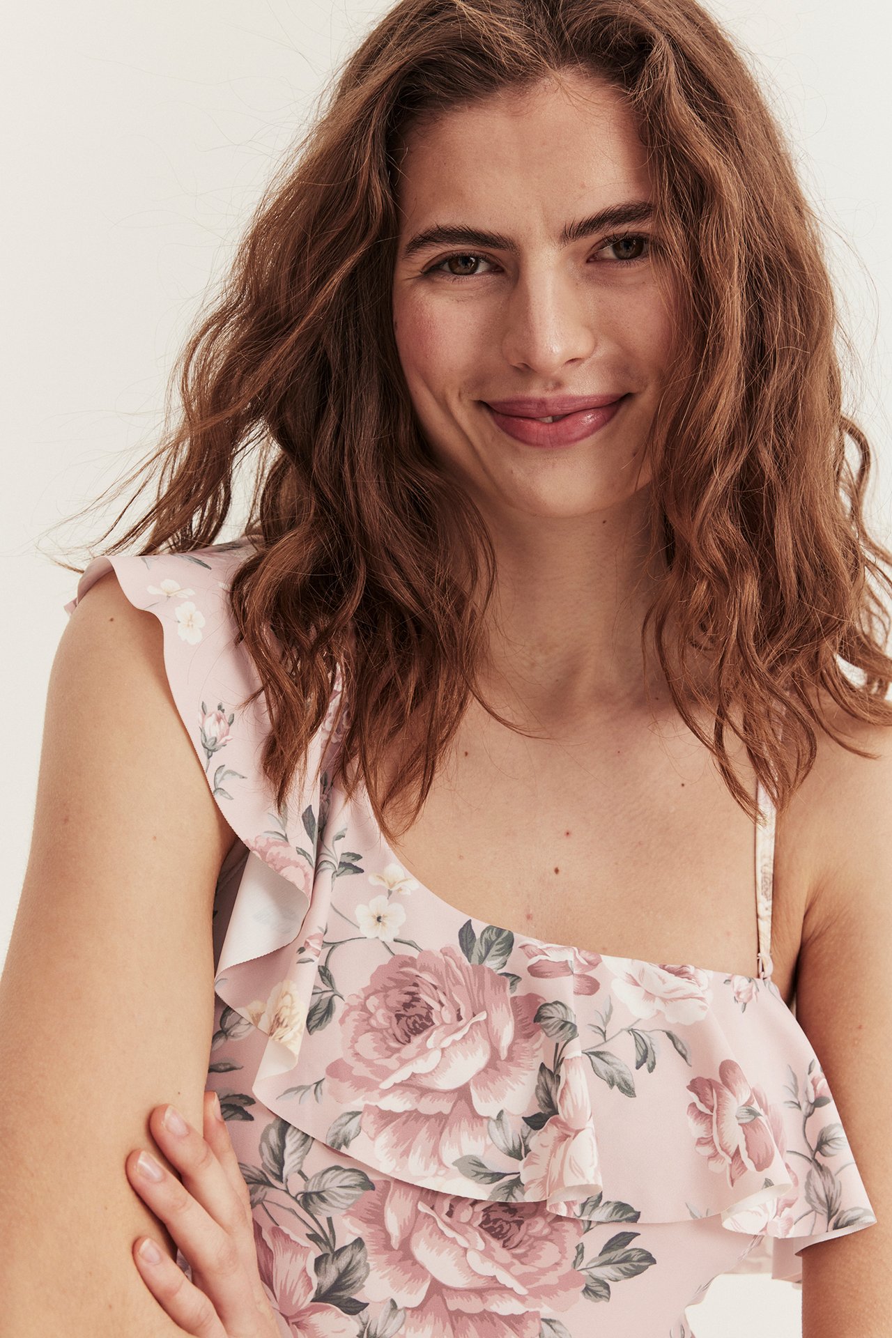 Close-up front view of a woman wearing a pink floral swimsuit with an asymmetric ruffled neckline.