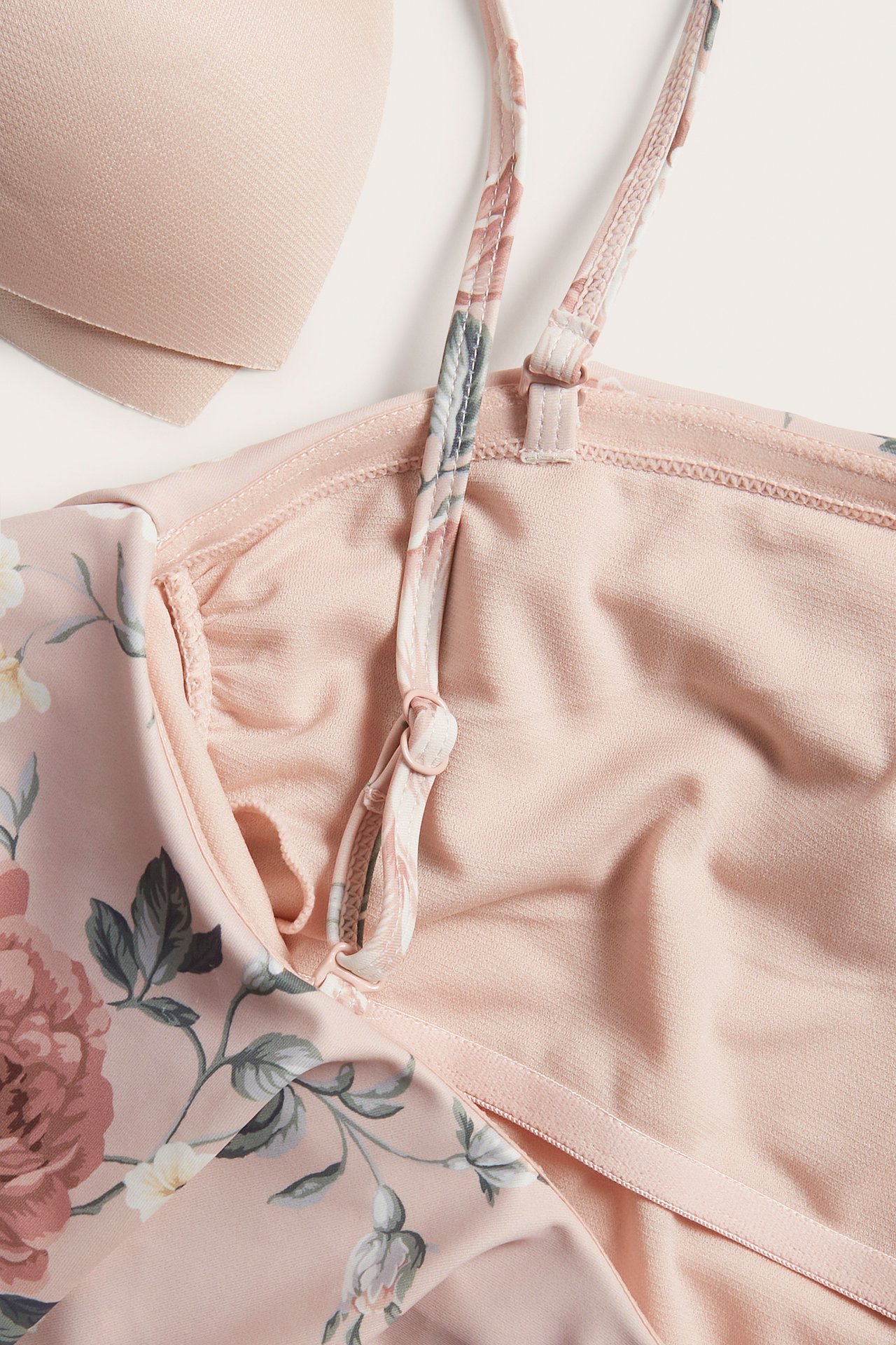 Close-up of a pink floral swimsuit with an adjustable strap, plain pink lining, and a removable bra pad.
