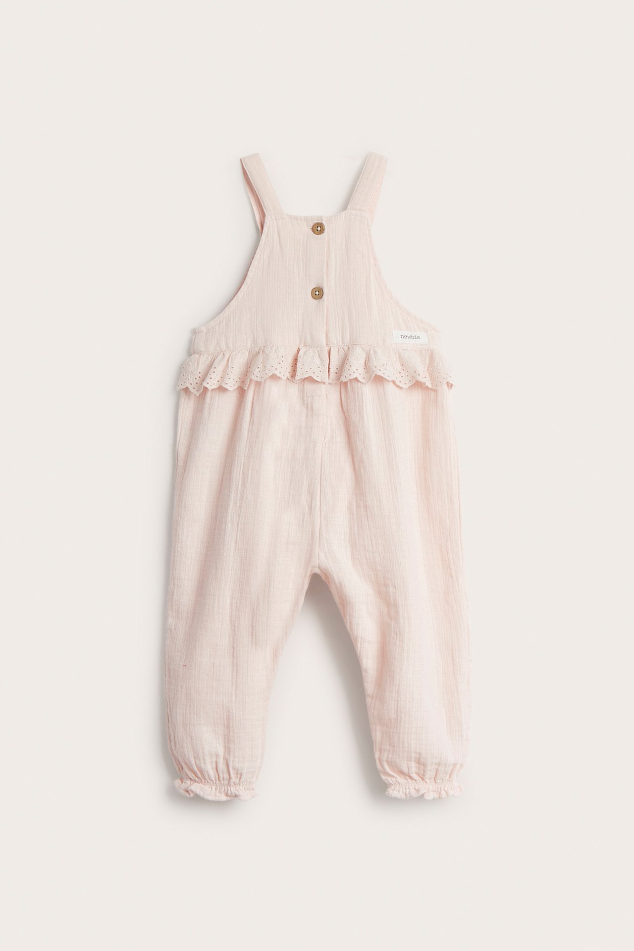 Vorderansicht hellrosa Baby-Latzhose aus Baumwollkrepp mit Spitzenrüsche, Bruststickerei und Knopfverschlüssen.