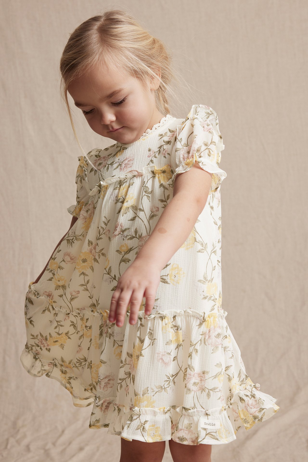 Vorderansicht eines Kindes in einem cremefarbenen geblümten Chiffonkleid mit Rüschen, Spitze und Puffärmeln.