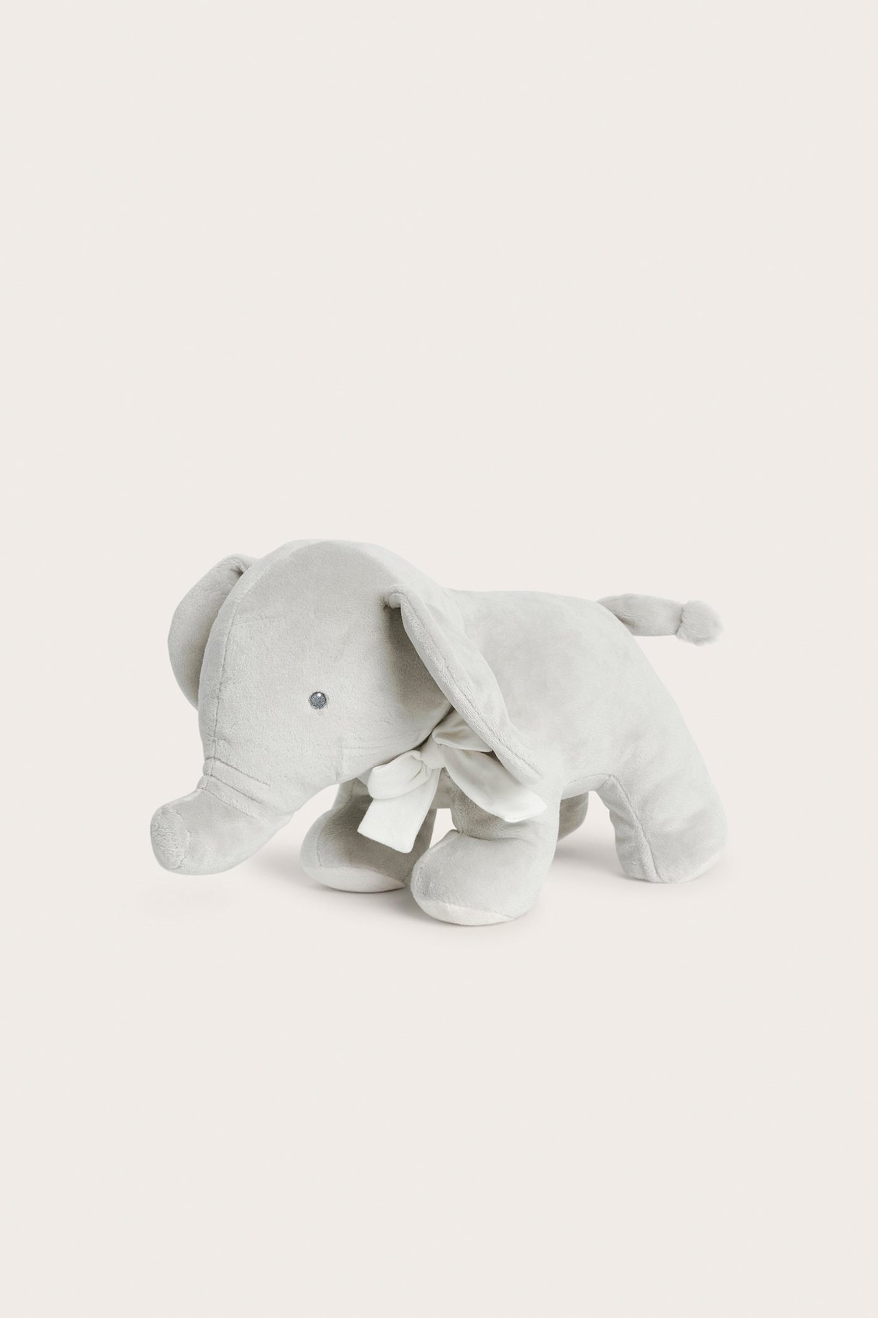 Front-side view of a light grey soft plush elephant stuffed animal with a white bow around its neck.