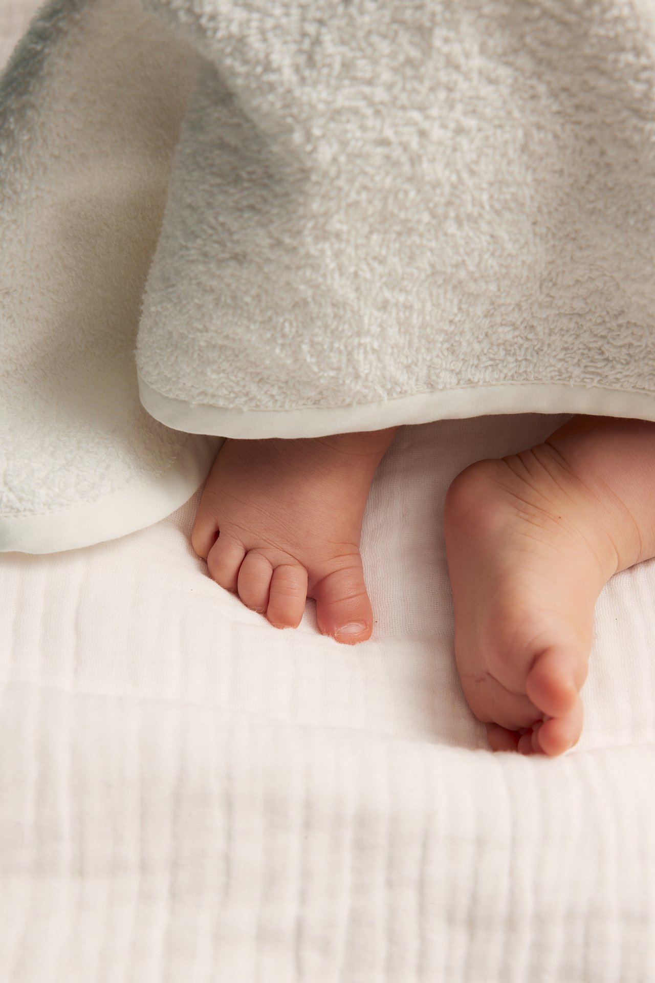 Nahaufnahme von Babyfüßen, die unter einem weichen, cremefarbenen Frotteehandtuch hervorlugen.