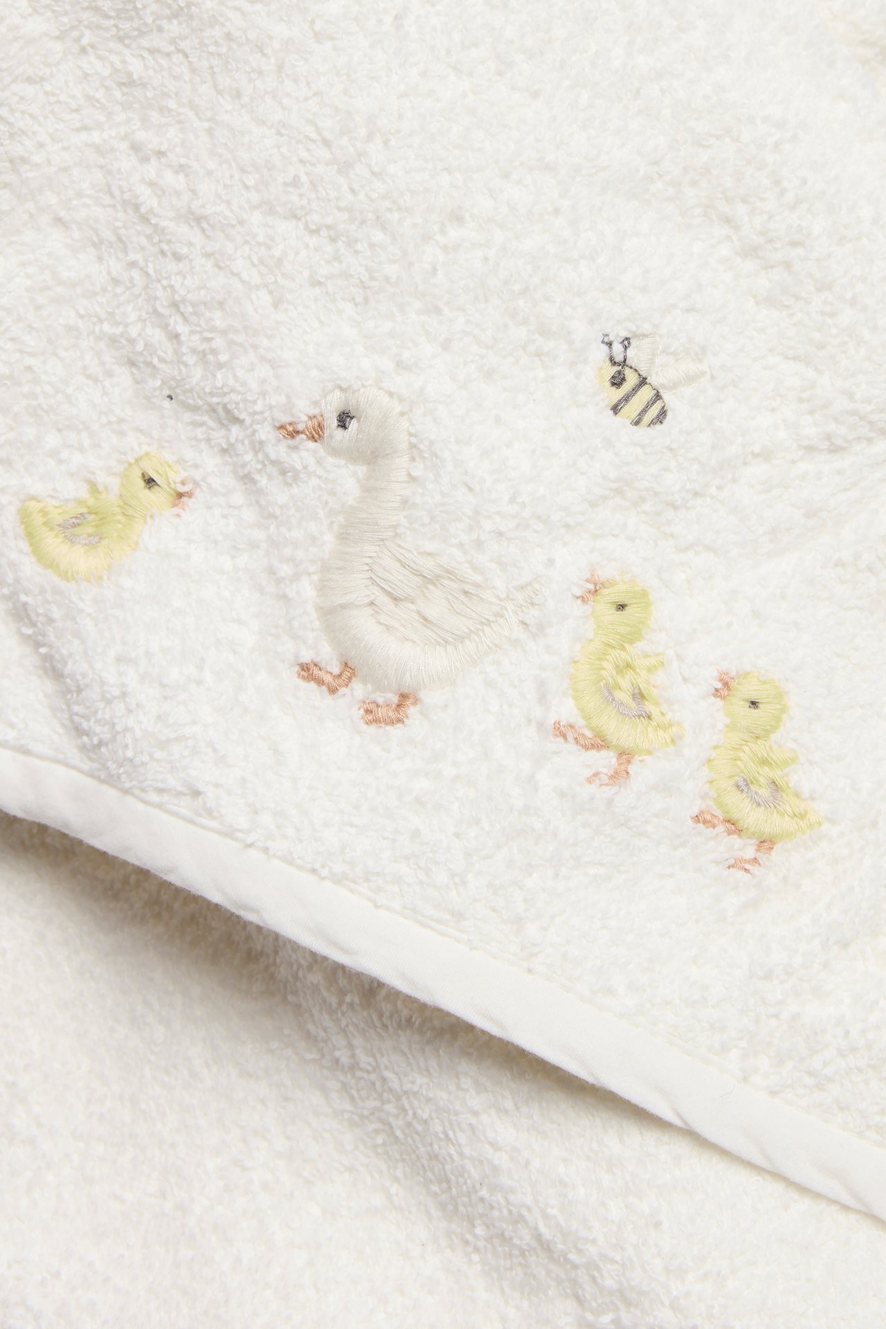Nahaufnahme eines cremefarbenen Frottee-Baby-Kapuzenhandtuchs mit gestickter Ente, Entenküken und Biene.