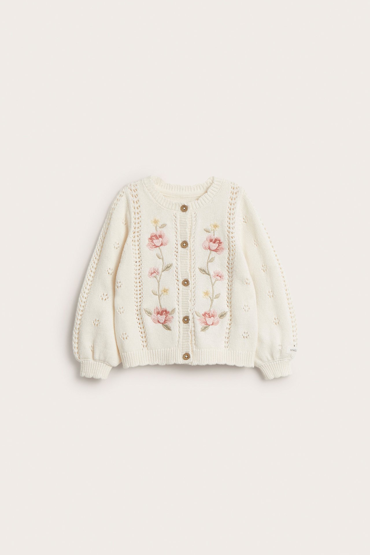 Front view of an offwhite kid's cotton cardigan with pink floral embroidery and brown buttons.