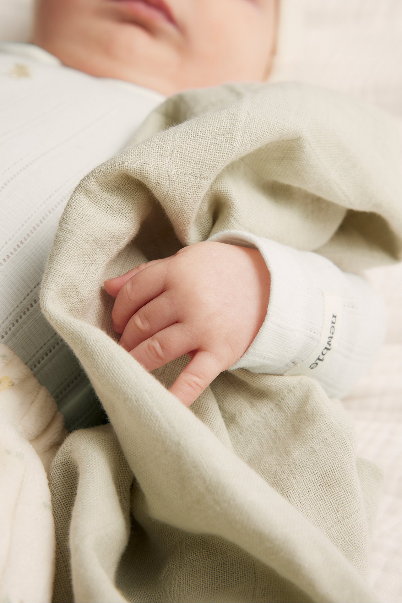 Close-up of a baby wearing an off-white pointelle rib long-sleeved body, with hand on a light green blanket.
