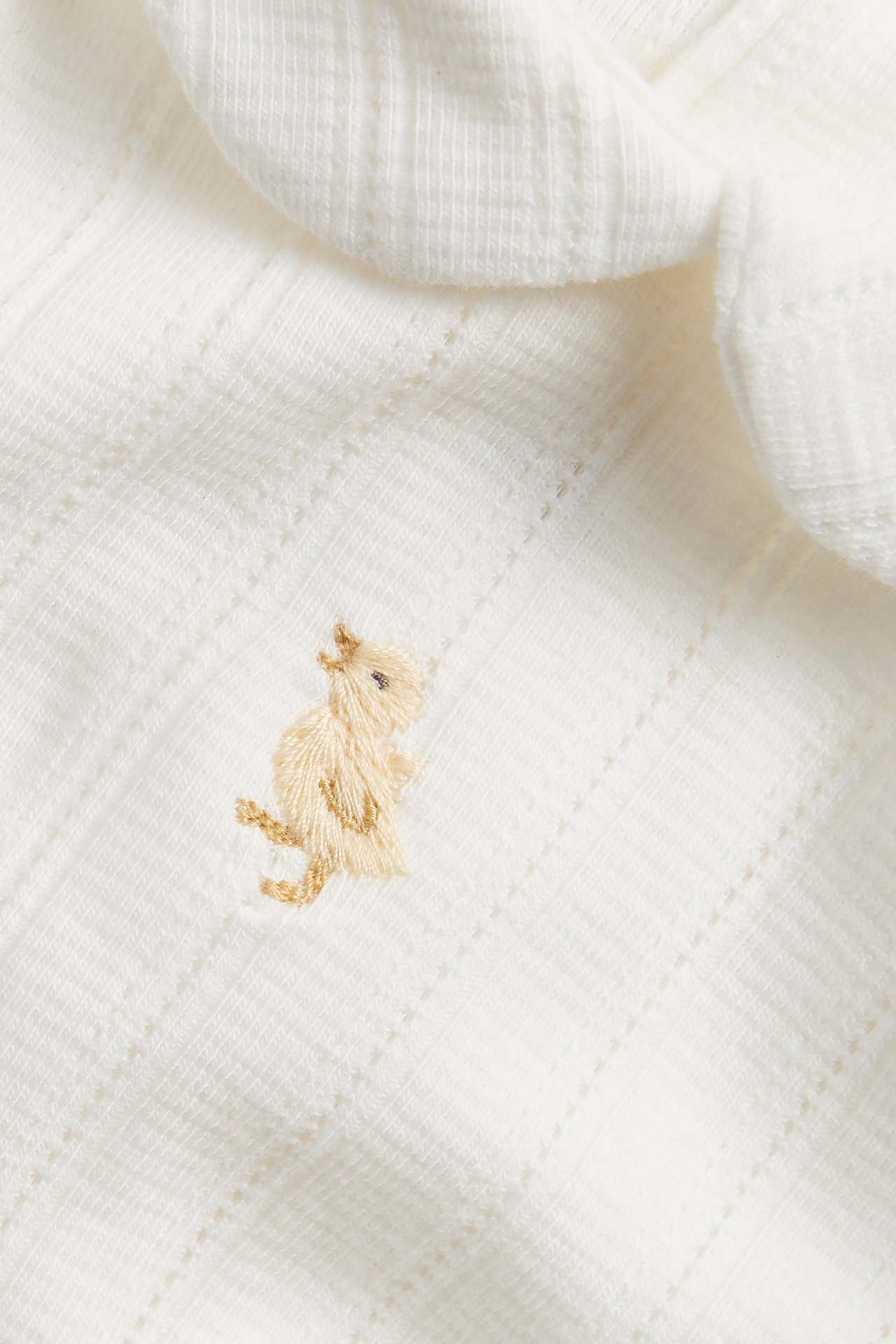 Close-up of an off-white baby pointelle rib bodysuit with a beige animal embroidery.