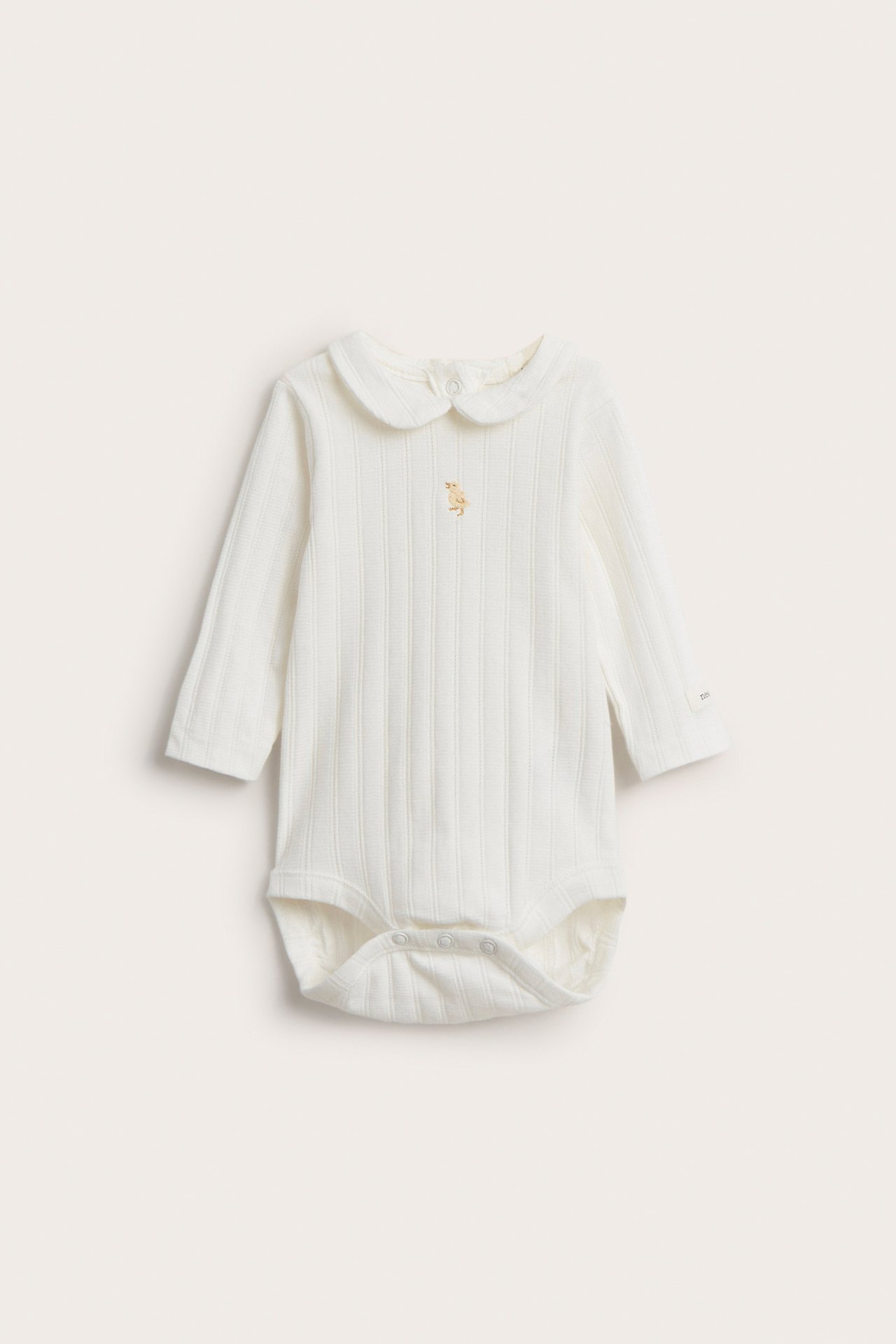 Front view of an off-white ribbed long-sleeved baby bodysuit with a collar and front embroidery, snap buttons.