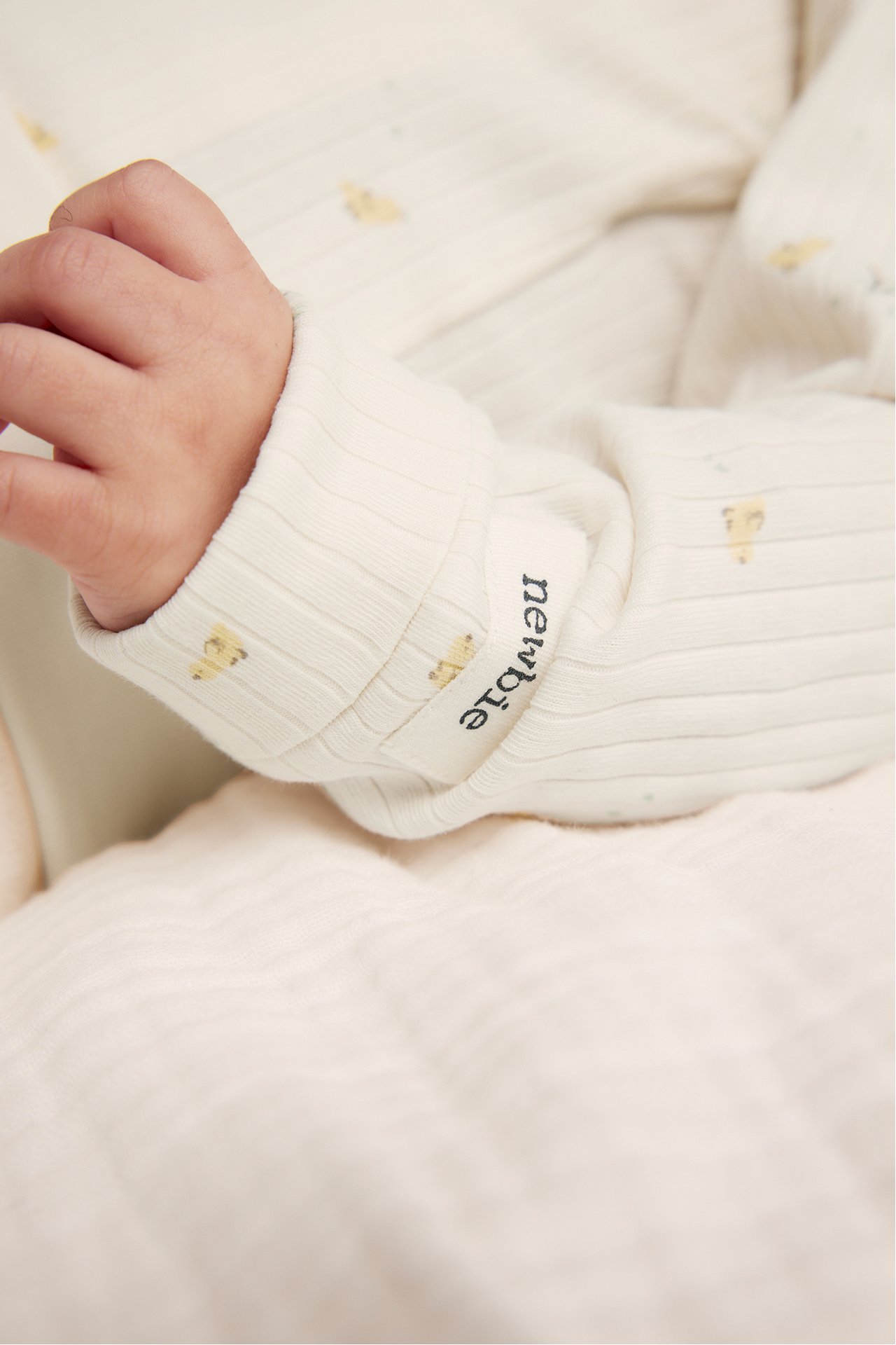 Close-up of baby's arm in an off-white ribbed cotton bodysuit with a small allover pattern.