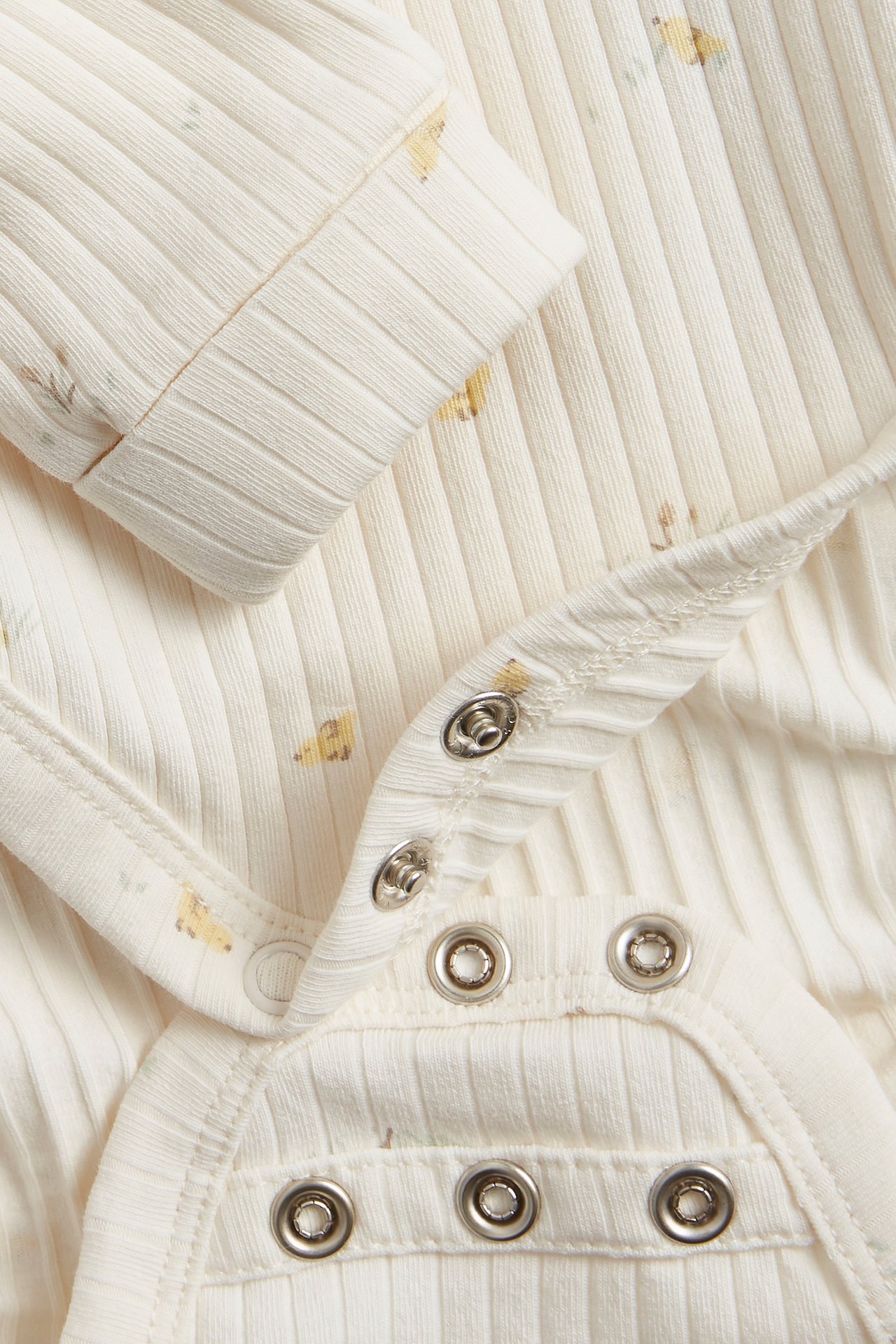 Close-up of an off-white ribbed baby wrap-around bodysuit with a subtle allover print and snap buttons.