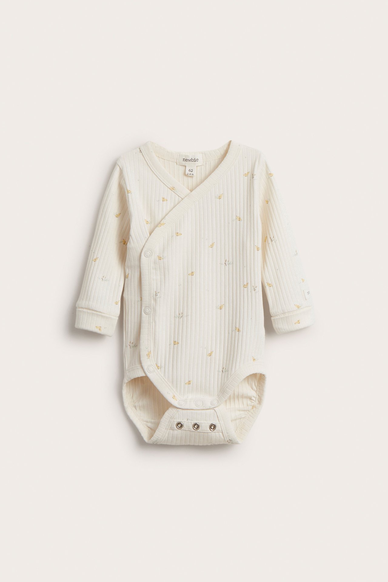 Front view of an off-white ribbed cotton baby wrap-around bodysuit with a subtle allover print and snap buttons.