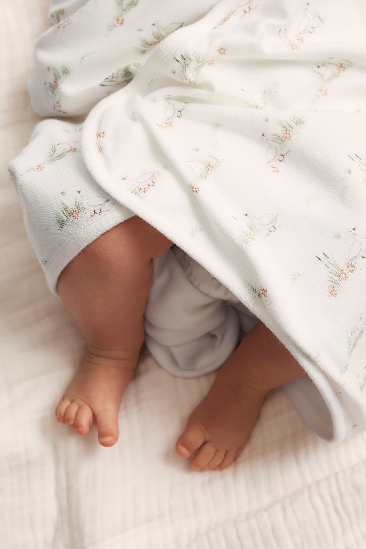 Nahaufnahme einer cremeweißen Baumwolldecke mit Entenmuster, die Babybeine bedeckt.