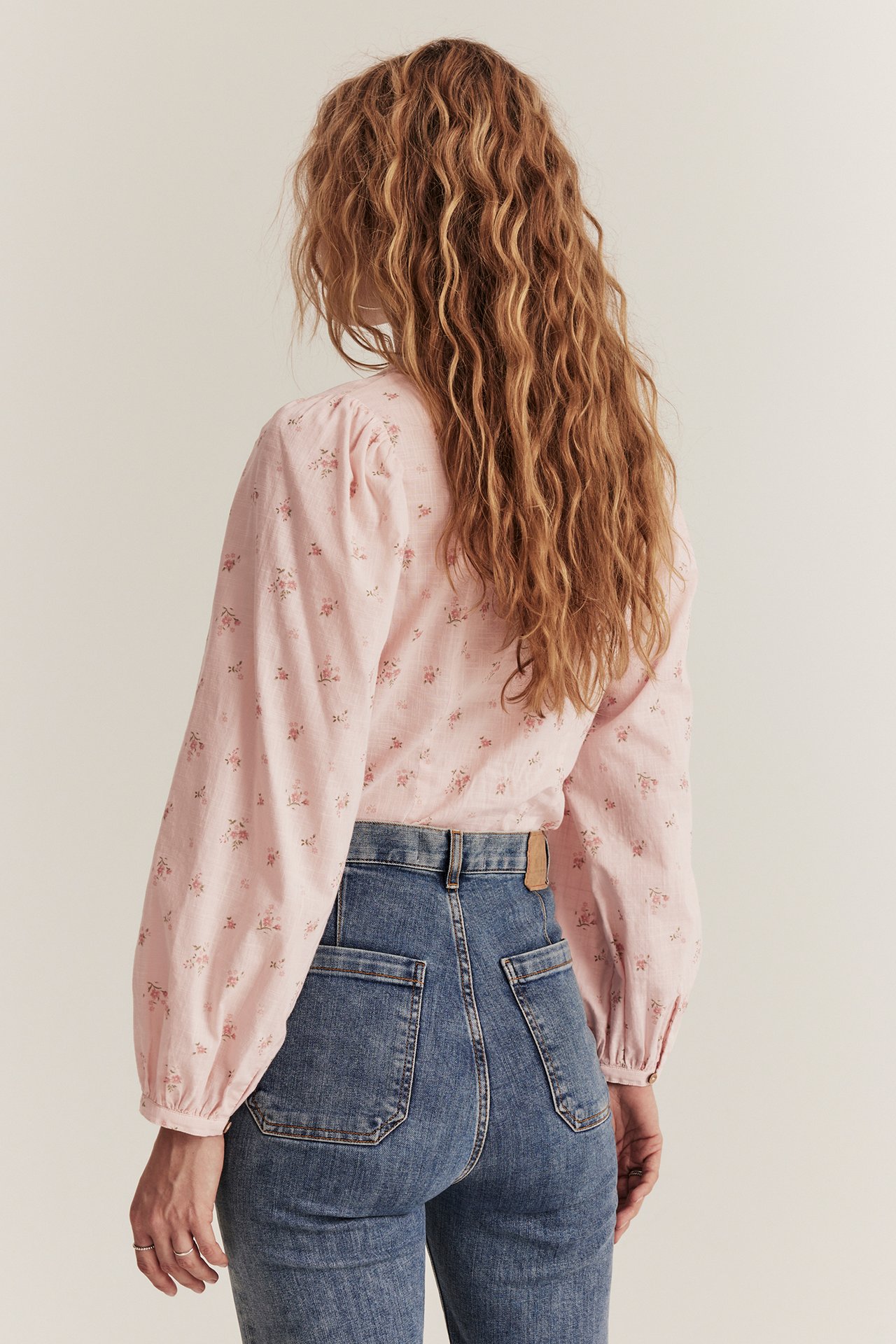 Rückenansicht einer Frau in hellrosa geblümter Baumwollbluse mit Puffärmeln und blauen Jeans.