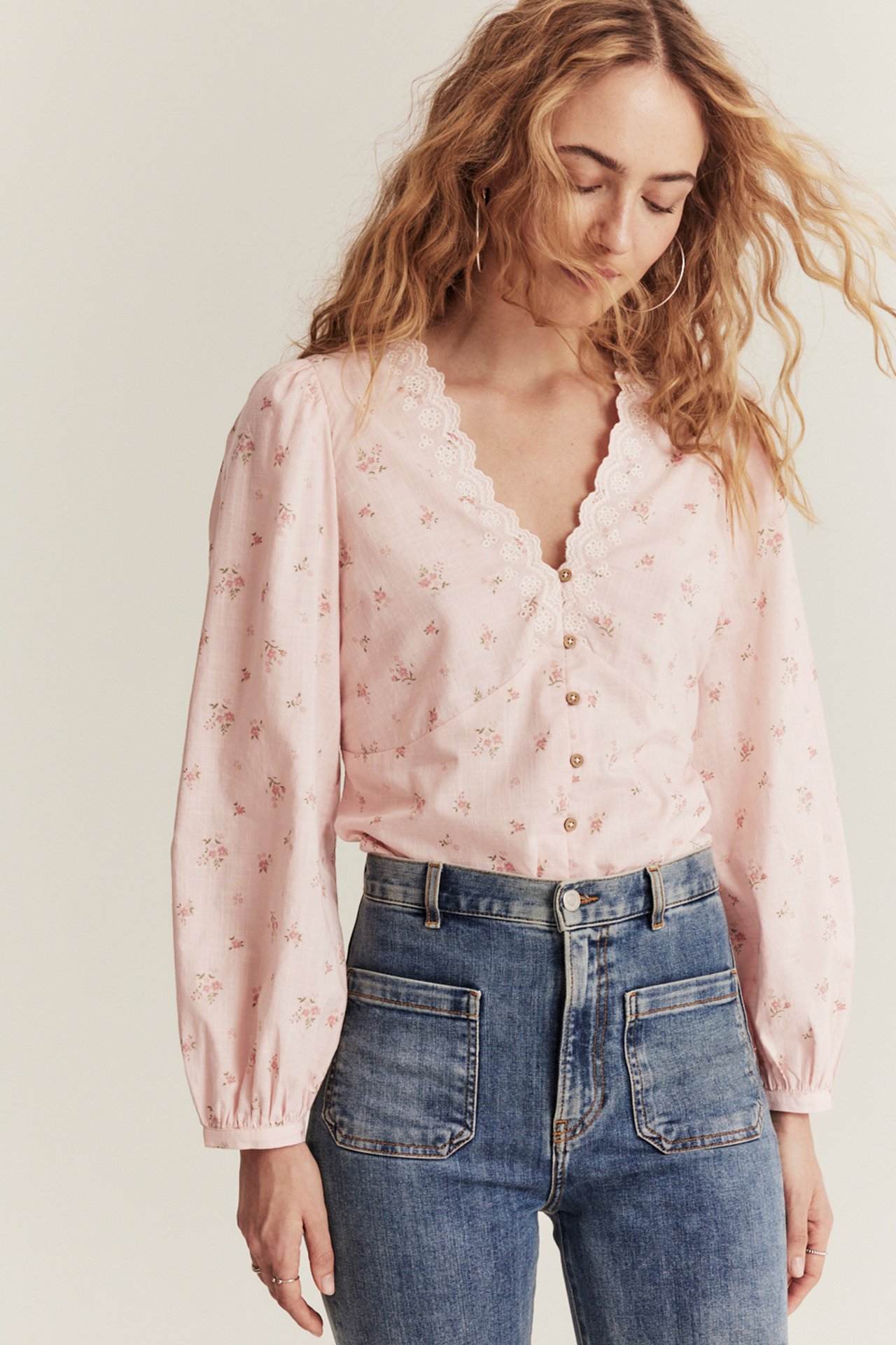 Vorderansicht einer Frau in hellrosa geblümter Bluse mit besticktem V-Ausschnitt und blauen Jeans.