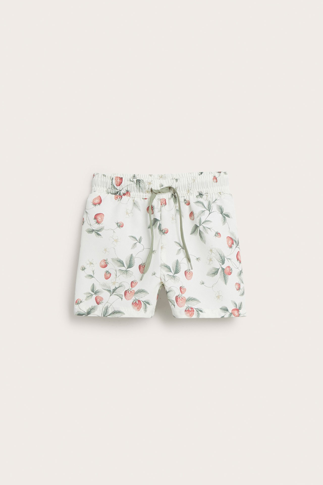 Vorderansicht von cremeweißen Baby/Kinder Badeshorts mit Erdbeermuster und grünem Kordelzug.
