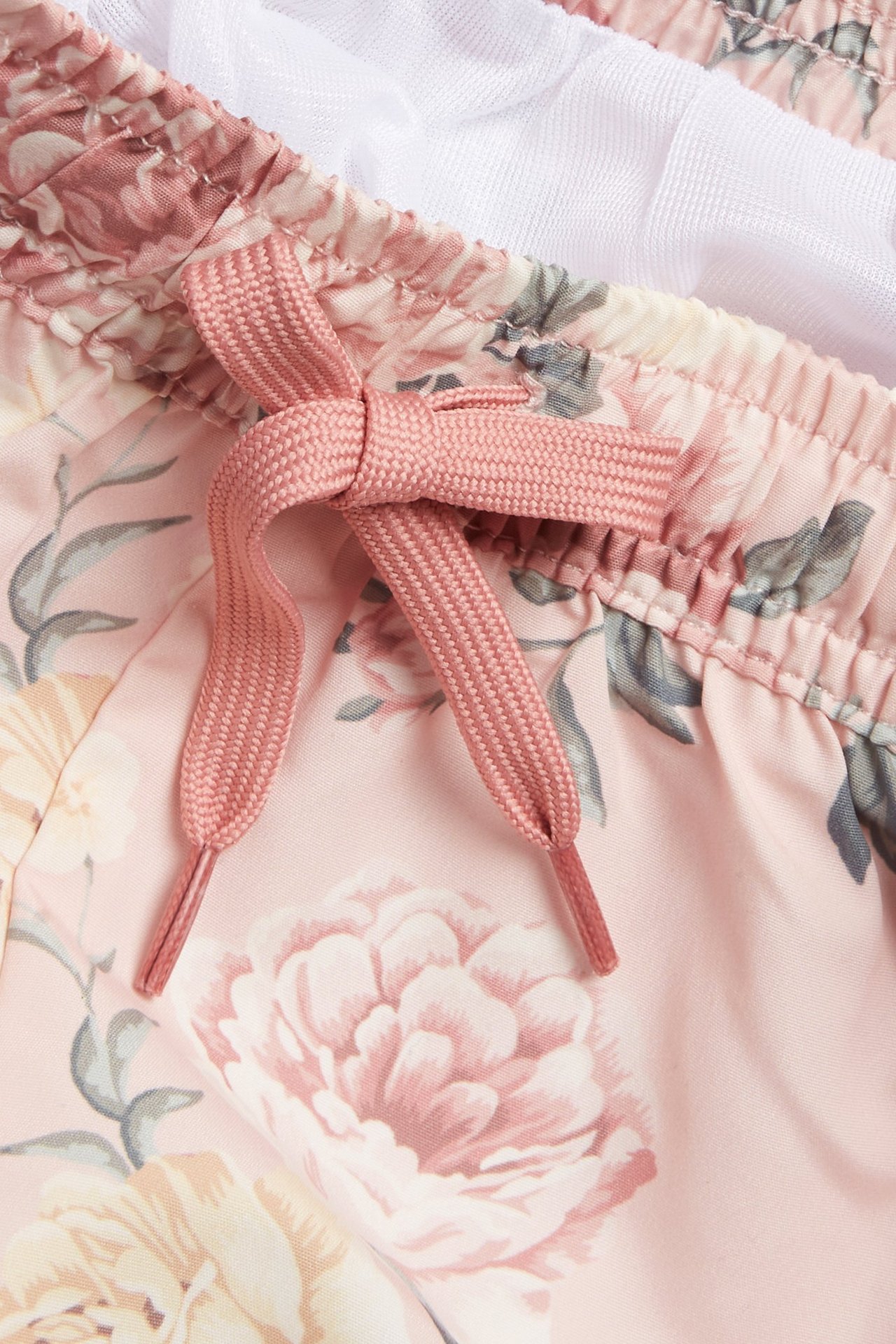 Nahaufnahme von rosa geblümten Baby-/Kinder-Badeshorts mit rosa Kordelzug und weißem Netzfutter.