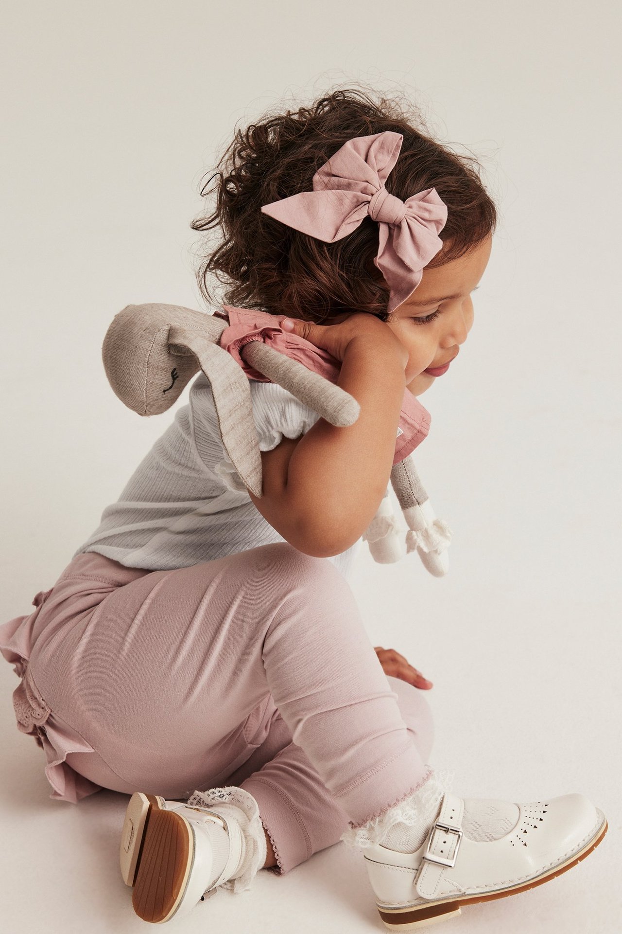 Side view of a kid in an off-white ribbed puff-sleeve body, pink leggings, white shoes, and a pink bow.