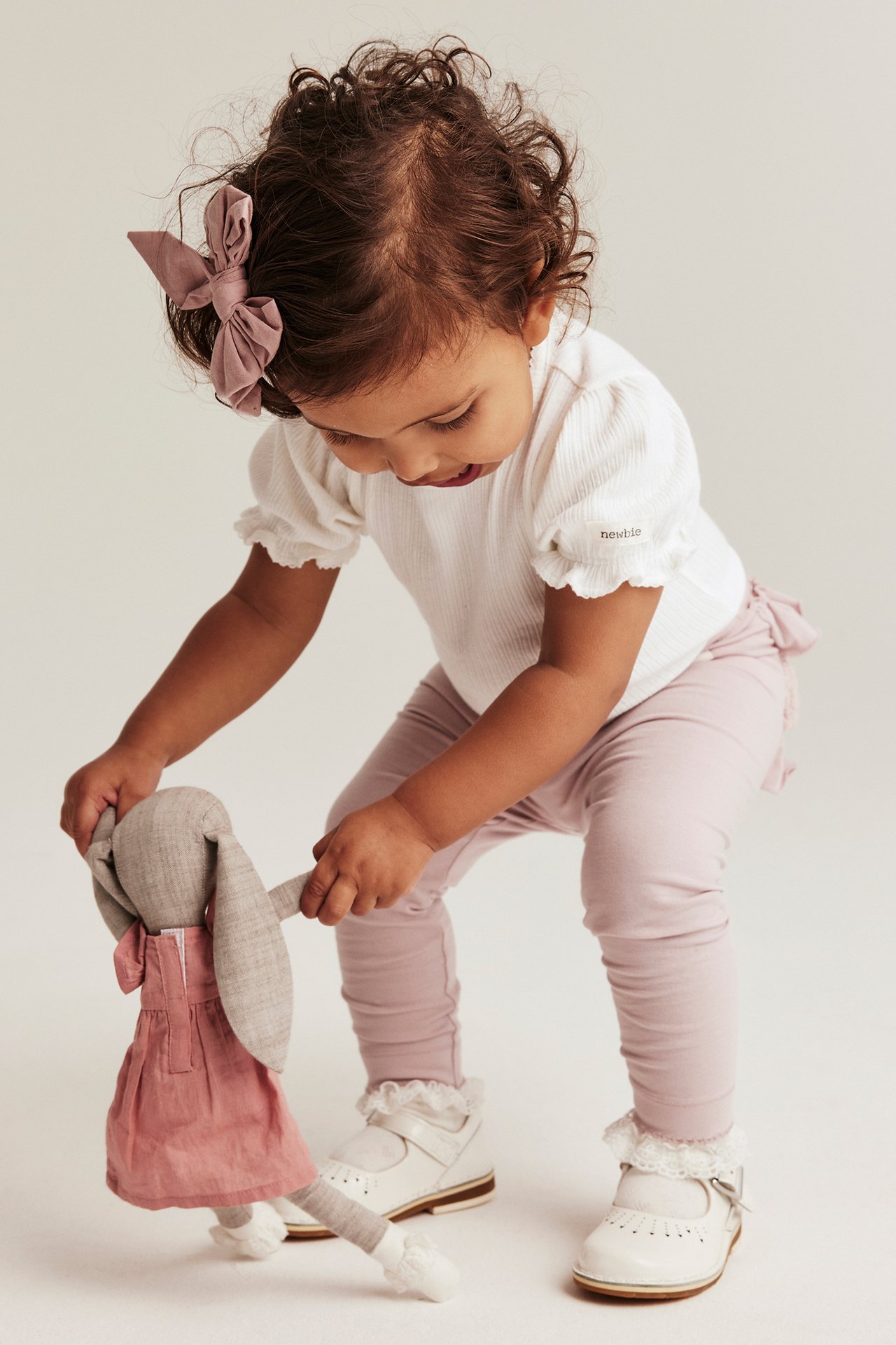 Baby in off-white ribbed bodysuit with puff sleeves, pink leggings, white shoes, and a pink hair bow.