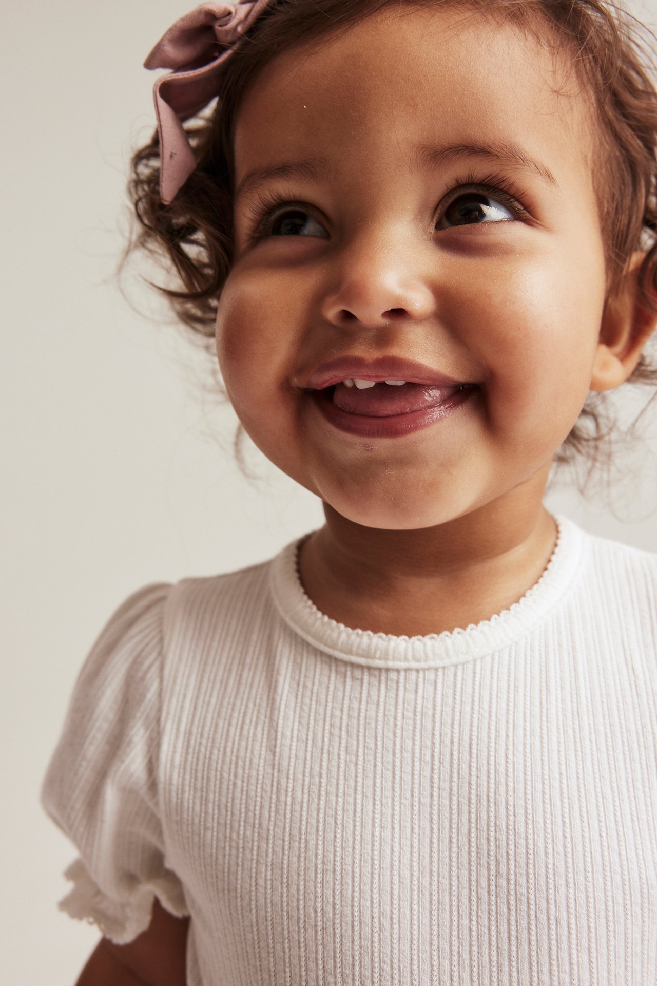 Close-up of a baby wearing an off-white ribbed jersey bodysuit with puff sleeves and a pink bow.