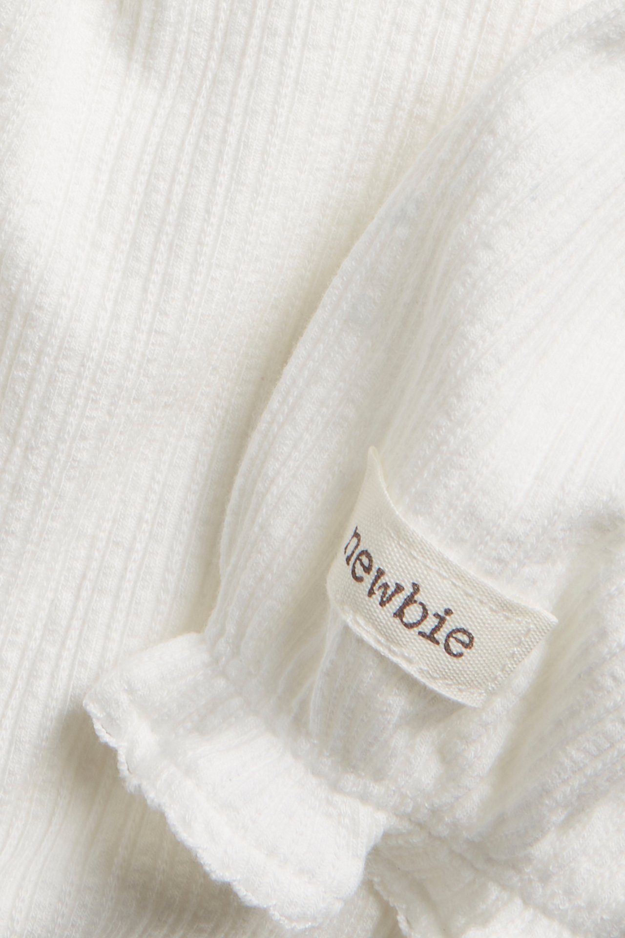 Close-up of an off-white ribbed jersey baby body with a short puff sleeve and picot edge.